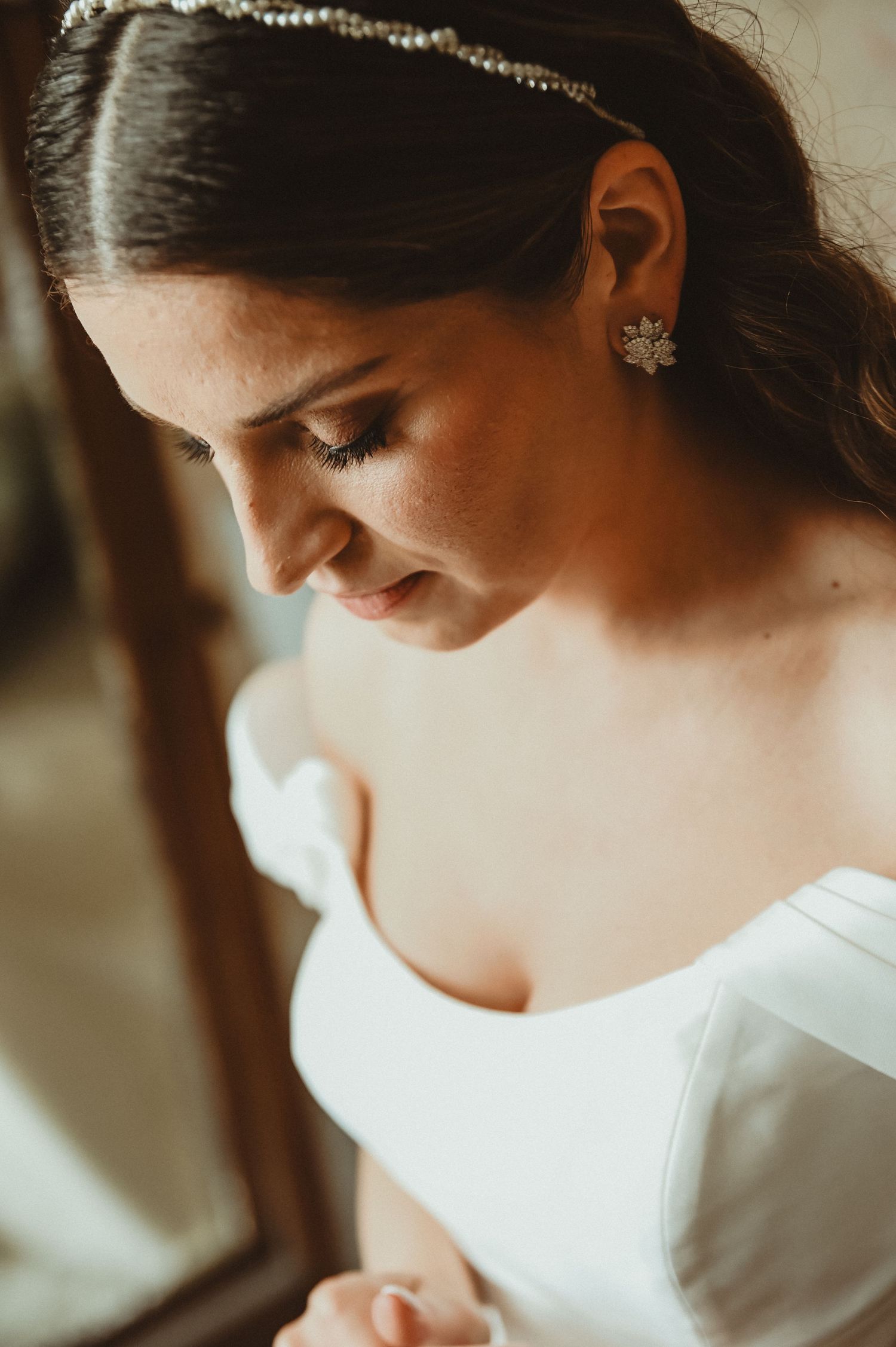 A close-up detail of delicate bridal jewelry and an off-shoulder white wedding dress.