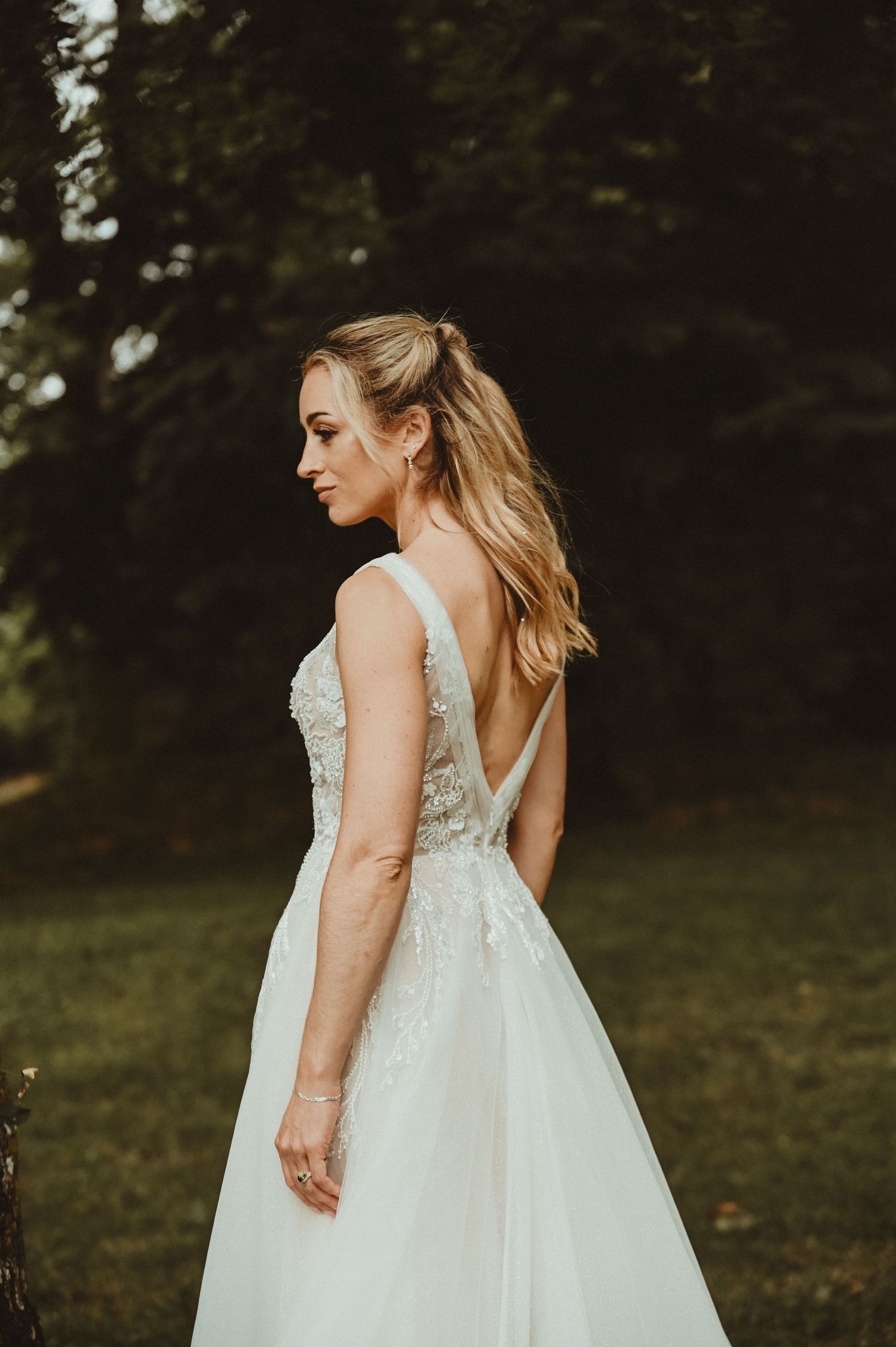 An elegant wedding dress with intricate lace details and deep V-back shown in moody outdoor setting.