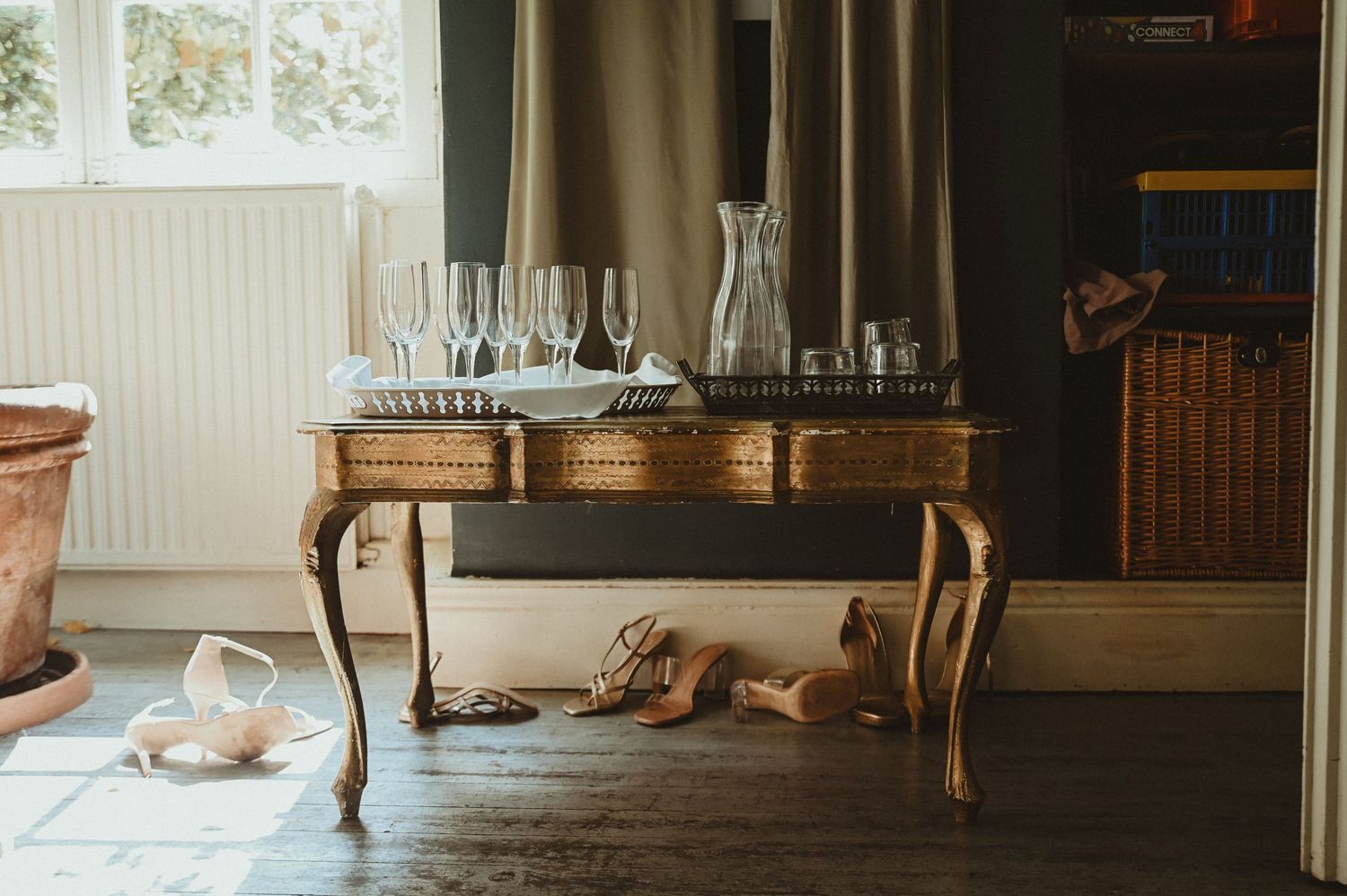 Elegant vintage table with glassware and carafe in a sunlit room with hardwood floors and draped curtains.