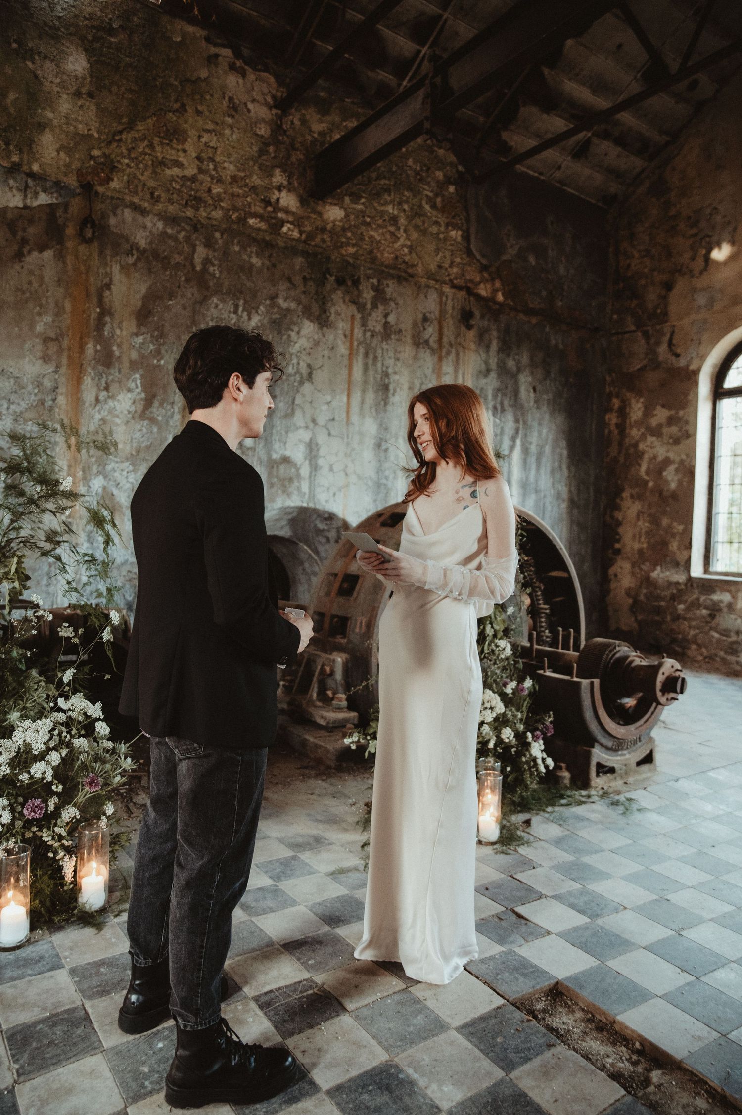 A wedding ceremony in an industrial venue with weathered walls and elegant candle lighting.