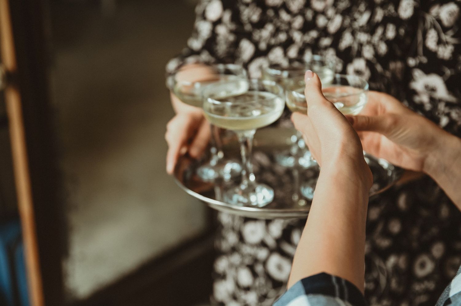 Two hands toasting with champagne coupes against a patterned background.