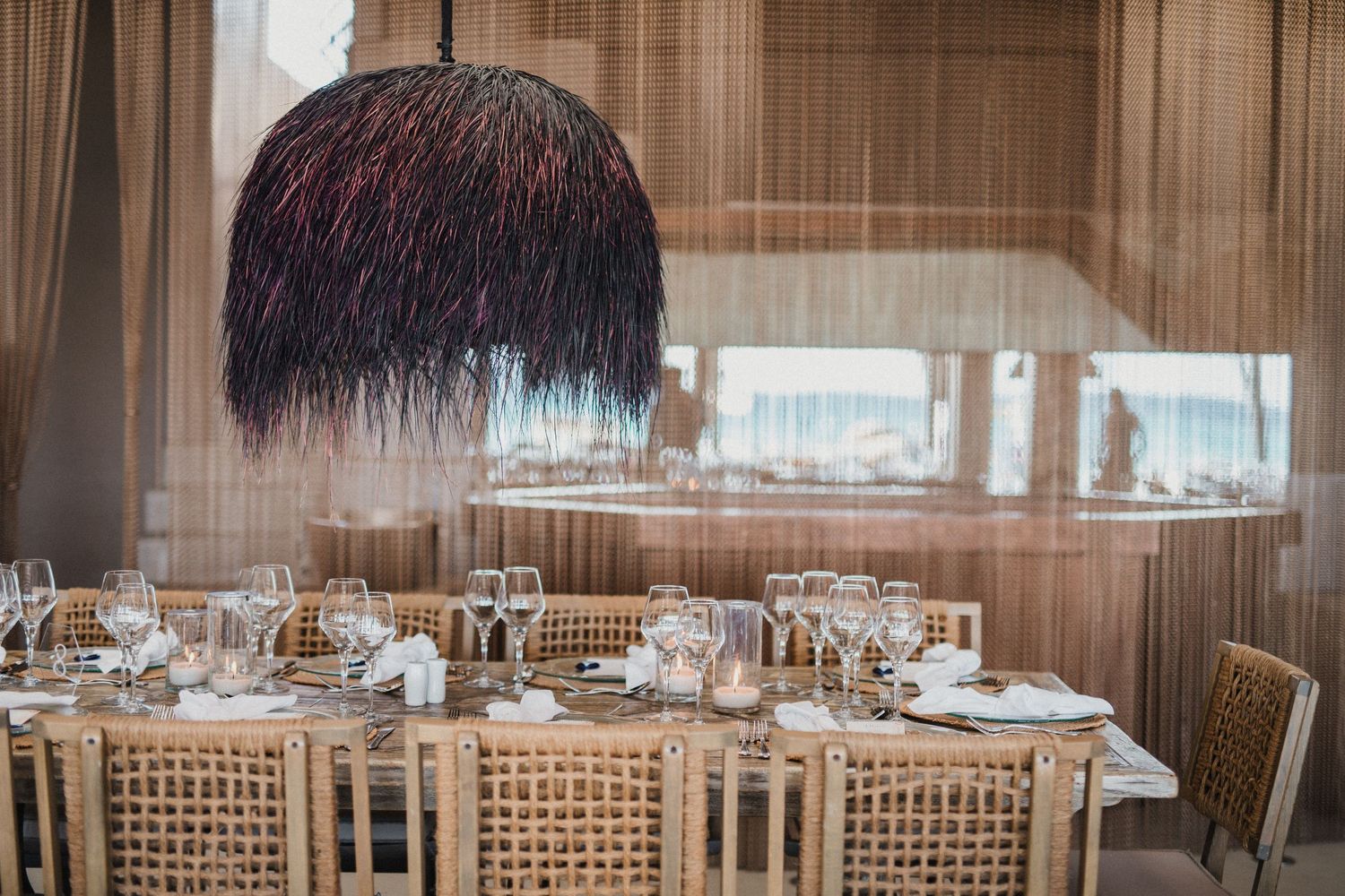 Modern restaurant table setting with dramatic black pendant light fixture and woven chairs.