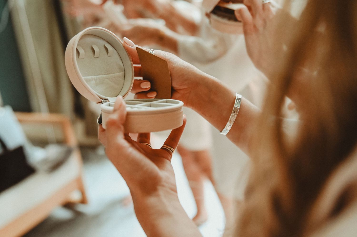 Hands hold open compact mirror in soft, dreamy lighting during wedding preparations.