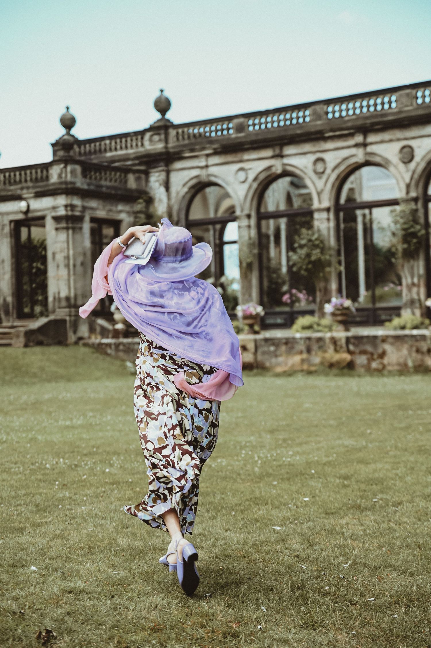 A person in flowing purple dress spins on grass in front of a classical stone building.