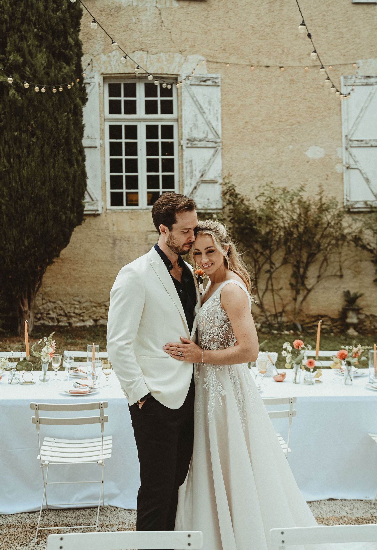 Romantic outdoor wedding setting with elegant table arrangements against a French country-style building.
