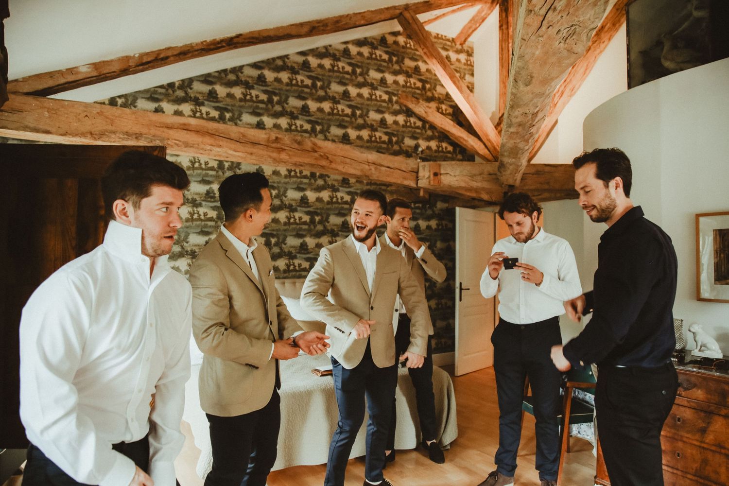 Group of men in formal attire gathered in rustic room with exposed wooden beams.