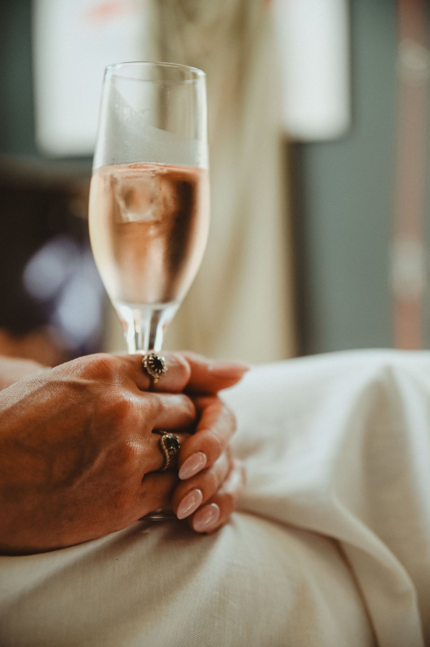 Hand holding a champagne flute with rose gold bubbles and wearing elegant rings.