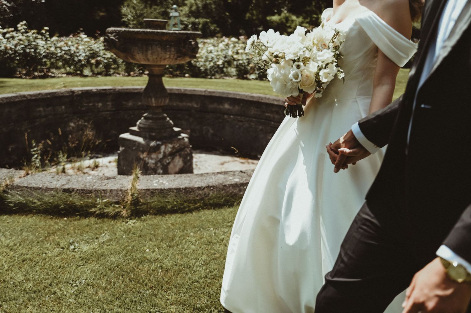 An artistic wedding photo featuring an ornate garden fountain and elegant attire.