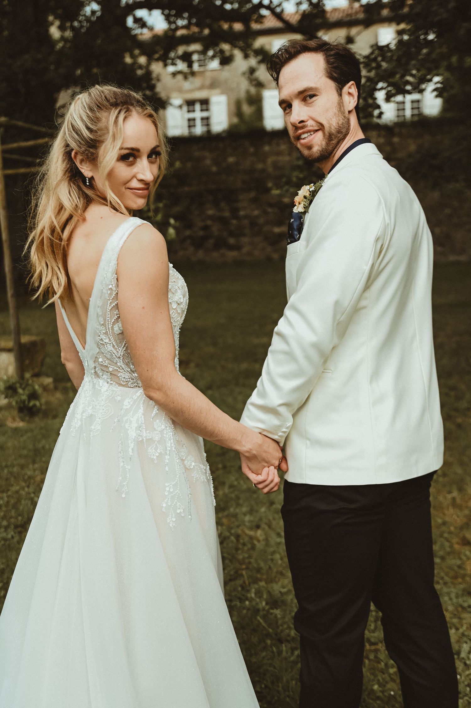 A romantic wedding portrait features the couple holding hands against a historic building backdrop.