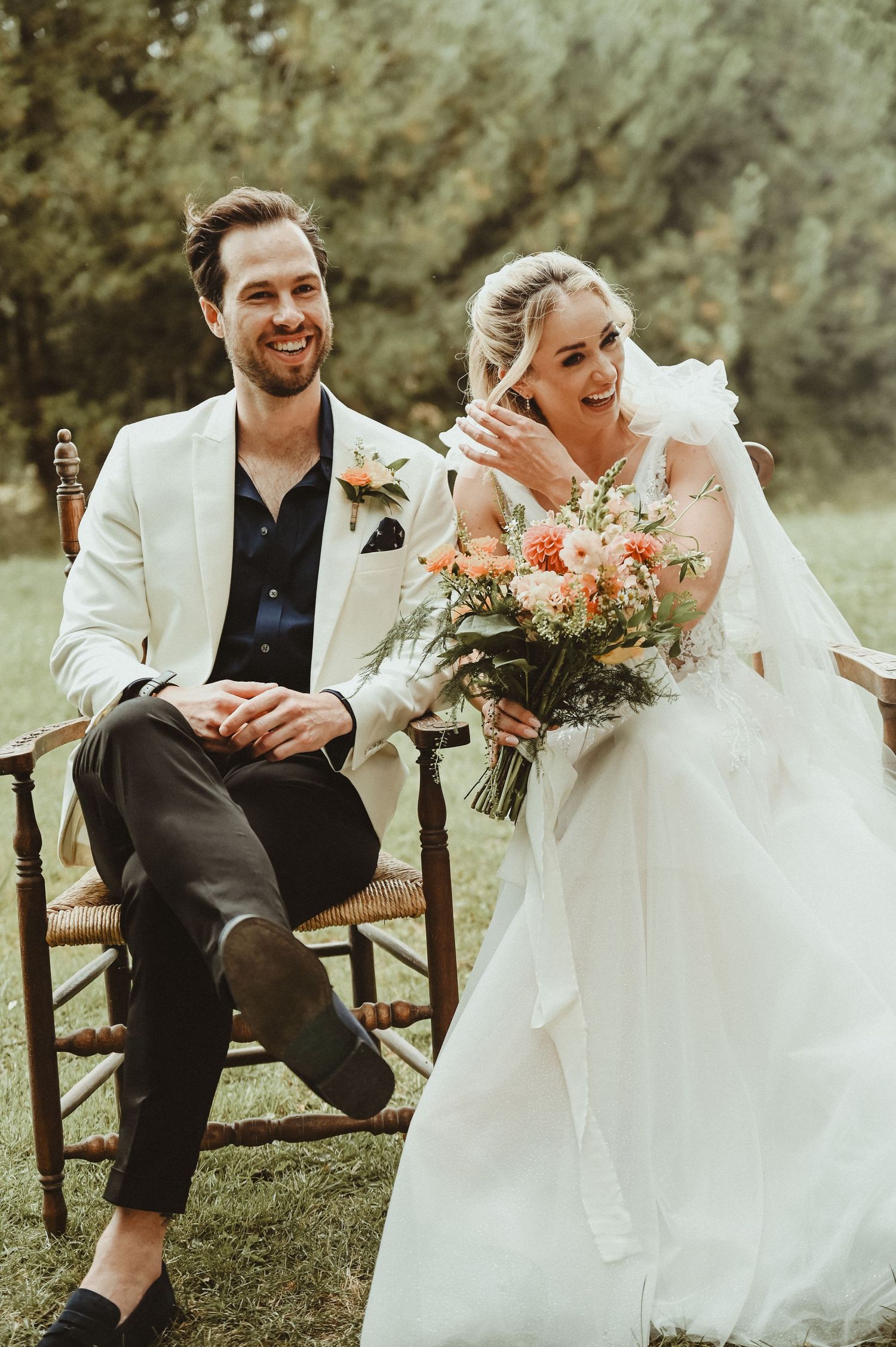 Newlyweds share a candid moment while seated on vintage chairs at their outdoor garden wedding.