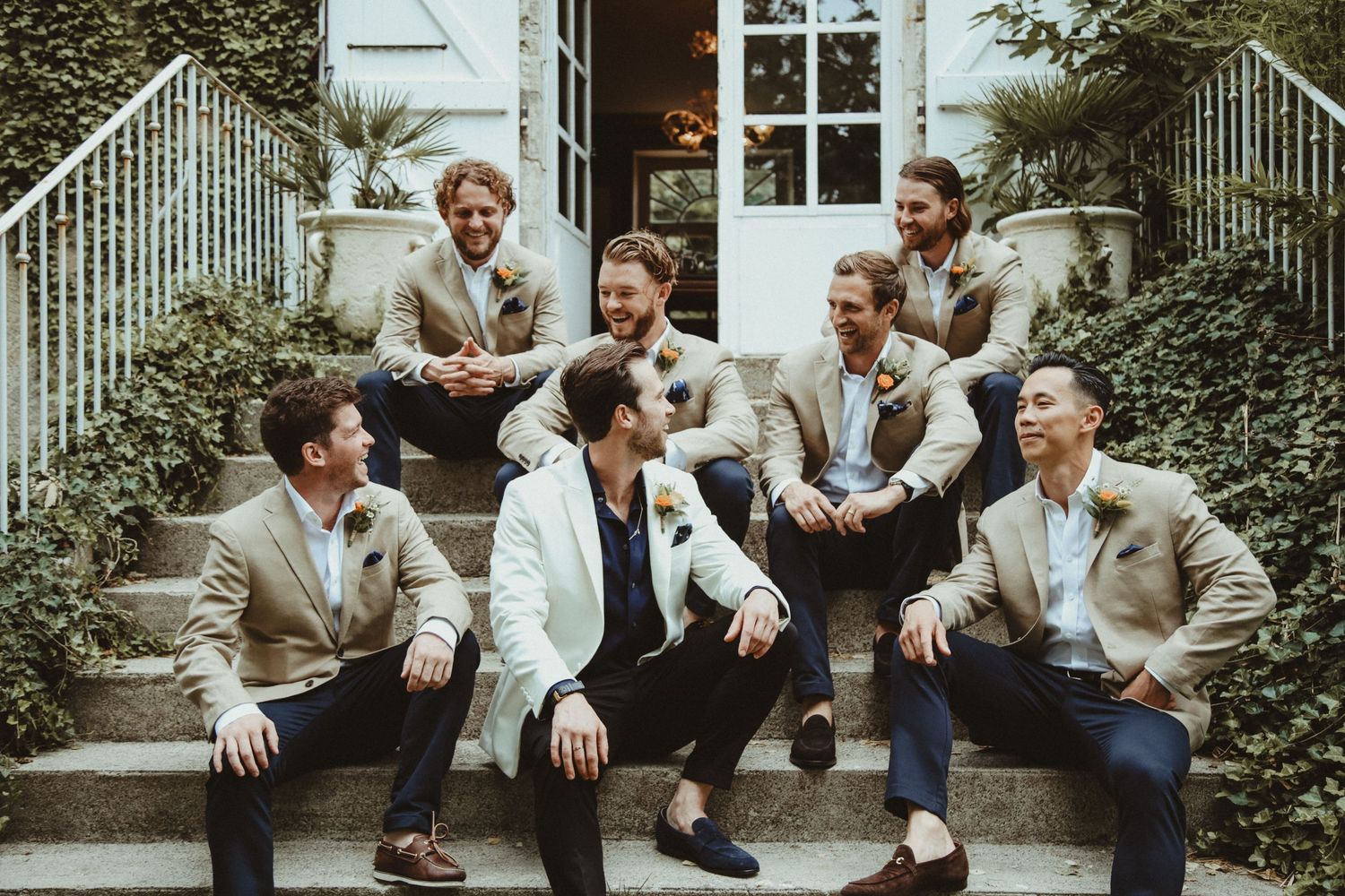 Wedding party relaxing on outdoor steps wearing coordinated beige and white suits.