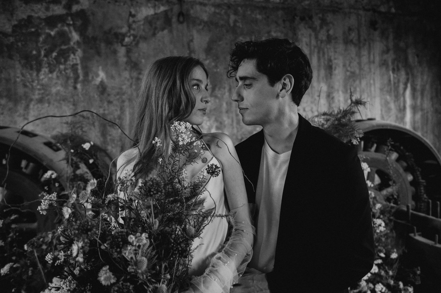 A black and white wedding portrait with floral arrangements in an industrial space.