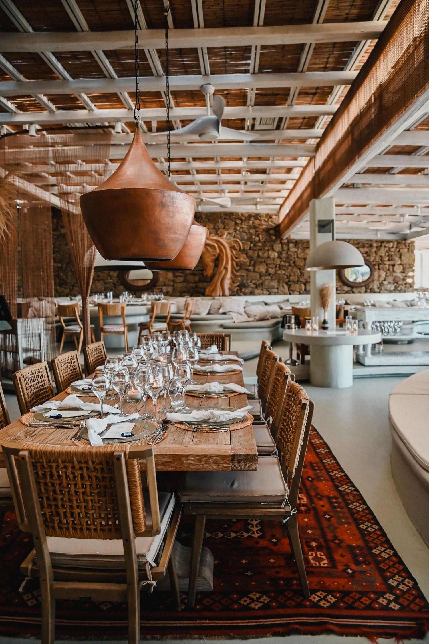 Rustic dining room with copper pendant lights and woven chairs on patterned rug.