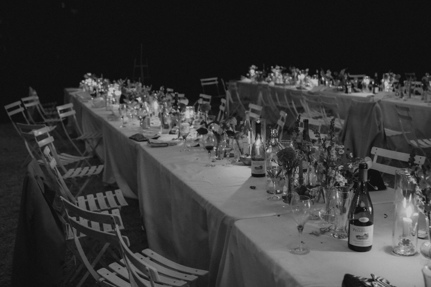 A long elegantly set wedding reception table with place settings and string lights overhead.