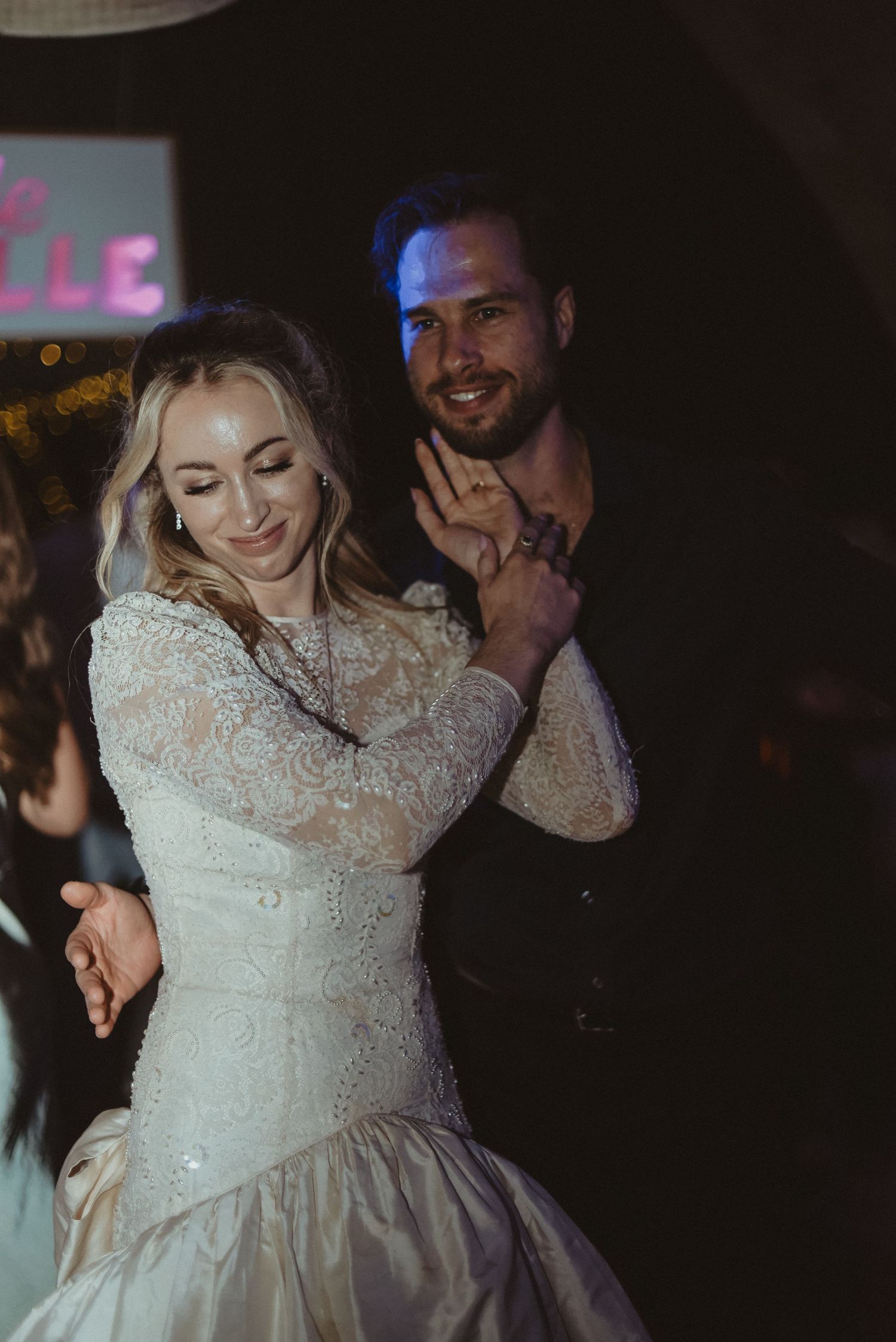 A couple dancing at their wedding reception, with the bride wearing an elegant lace dress.