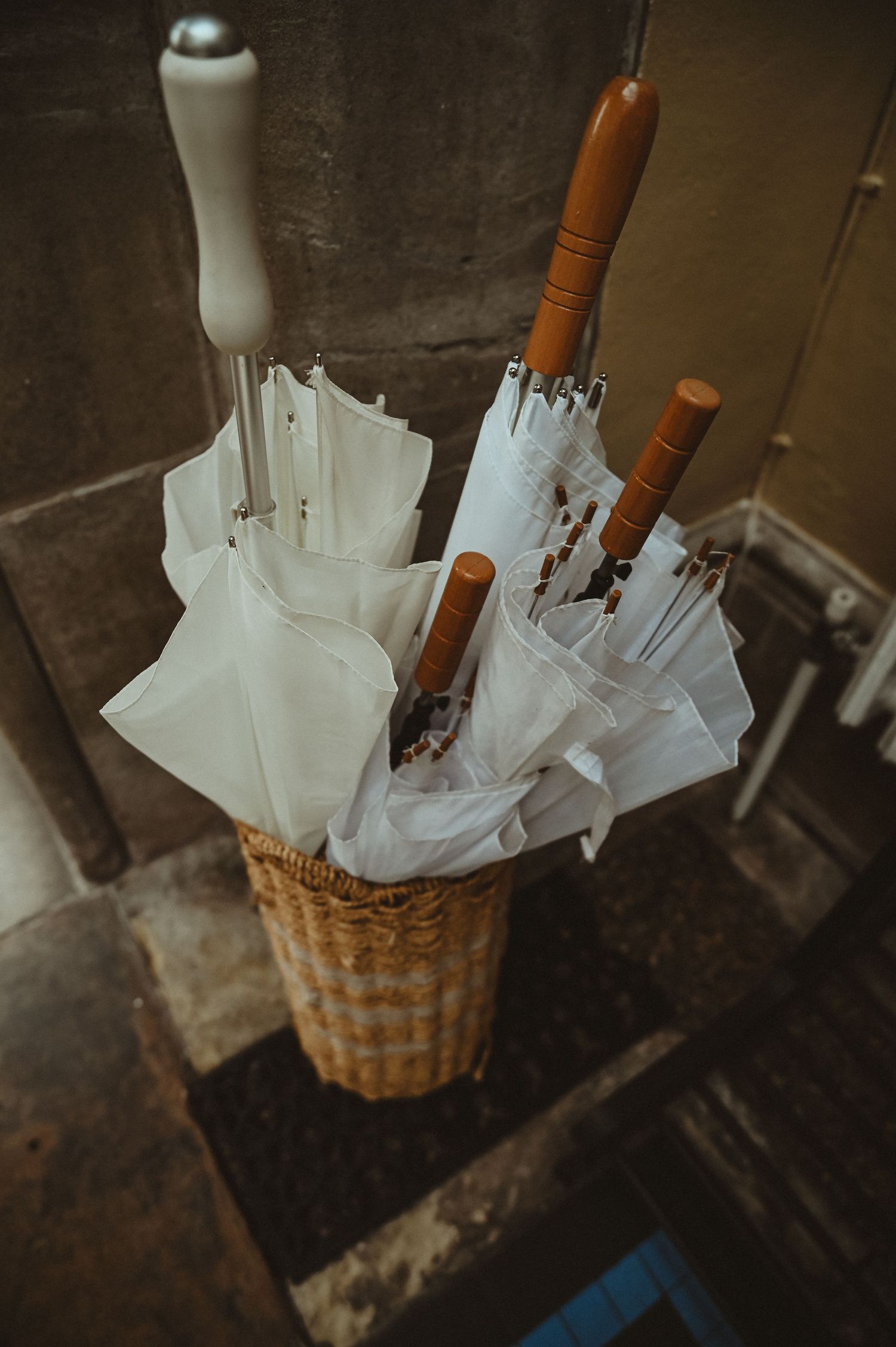 Collection of white umbrellas with wooden handles arranged in a wicker basket.