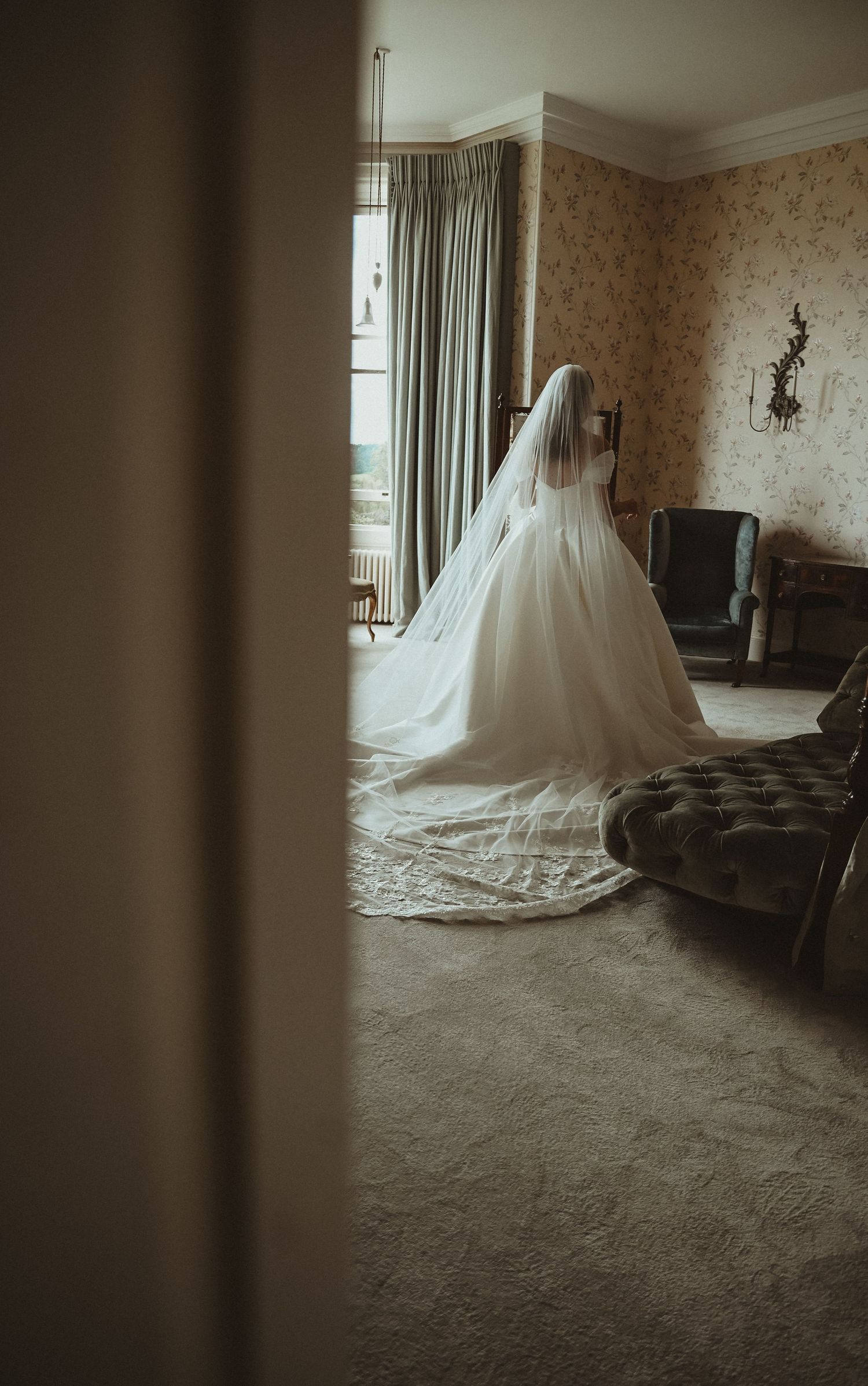 A wedding dress silhouette photographed through a doorway in a room with vintage decor.