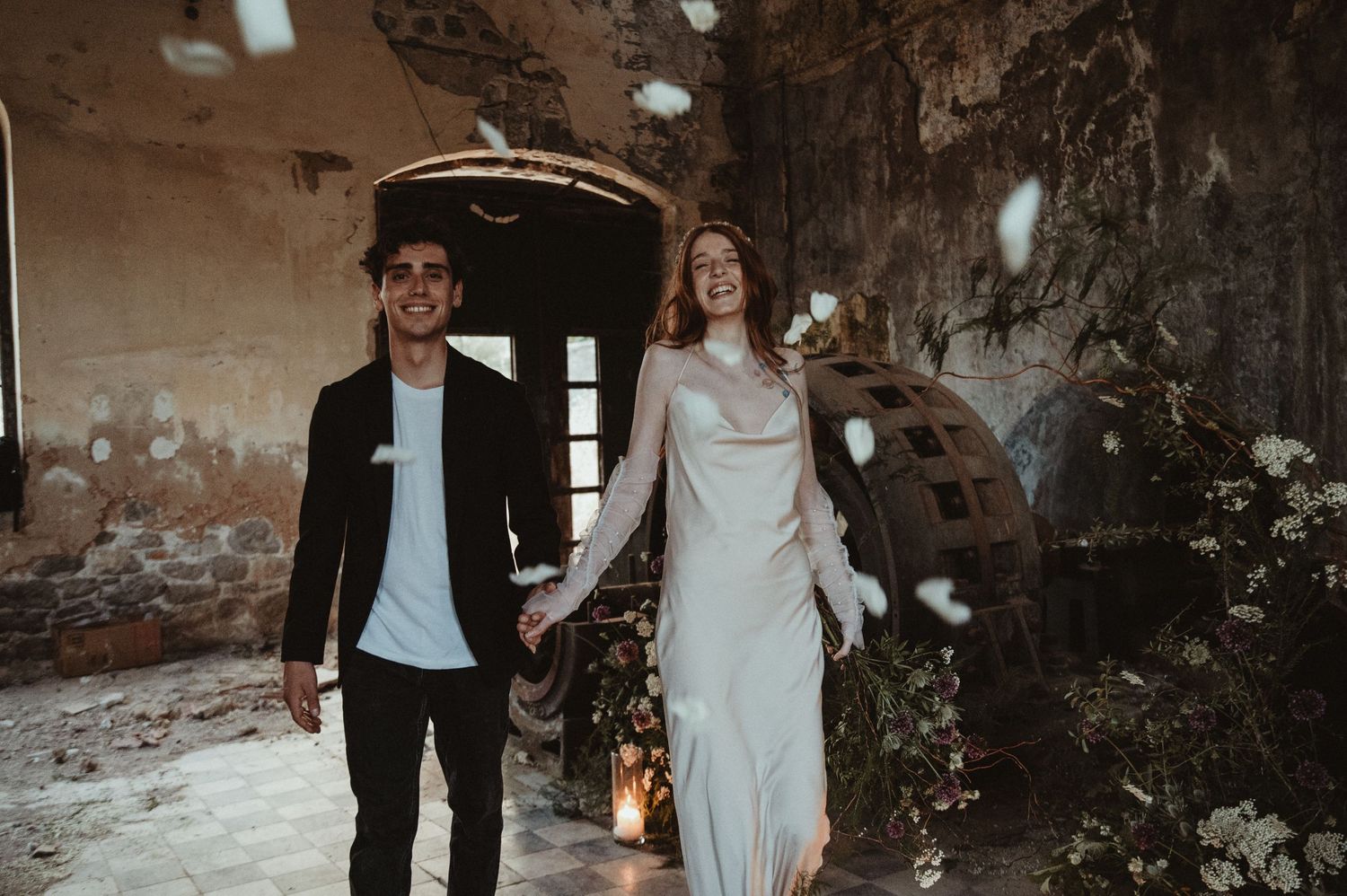 A couple walks hand in hand through a rustic industrial space with candlelit decor.