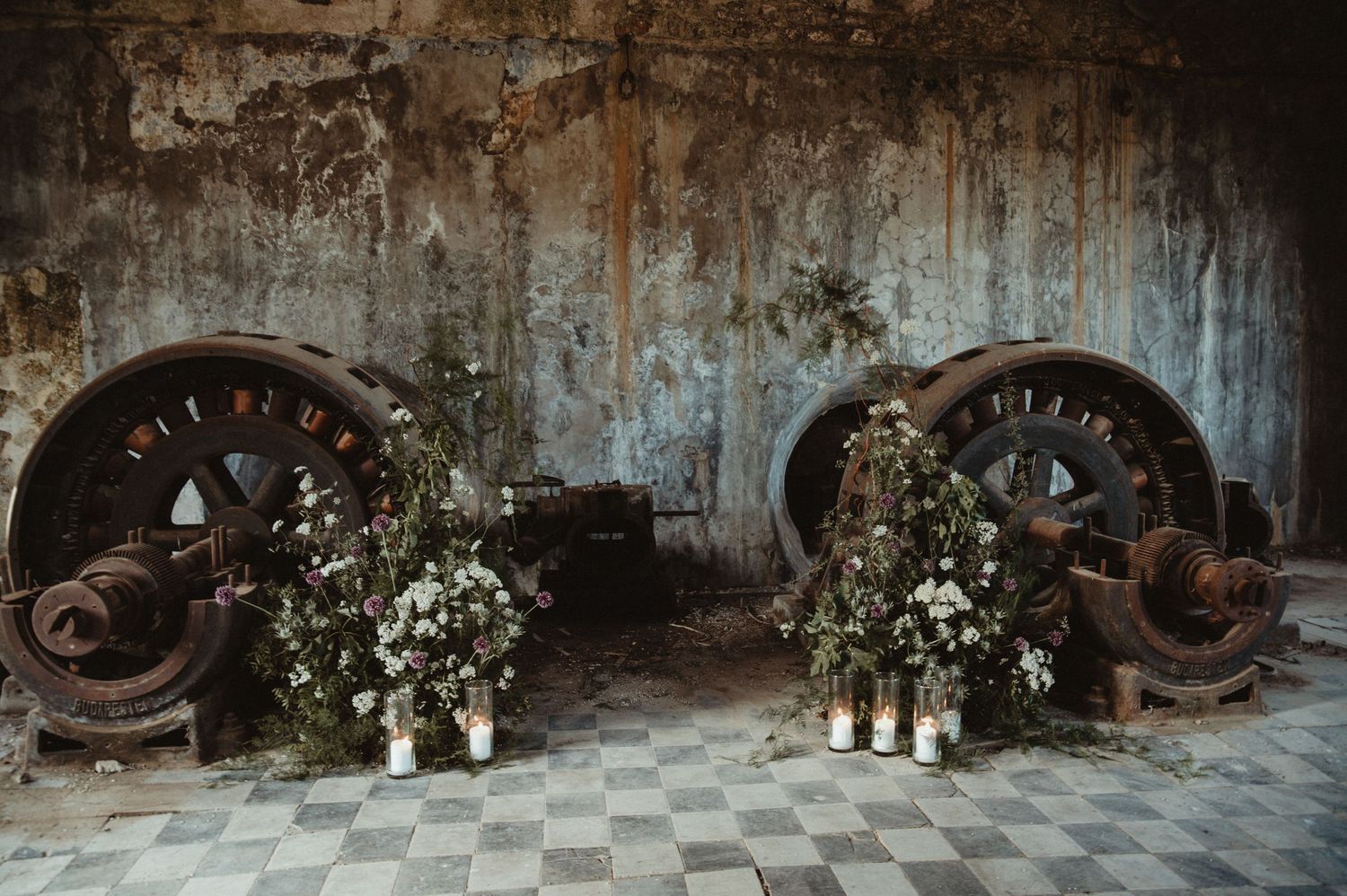 Industrial wedding venue decorated with white floral arrangements against weathered wall.