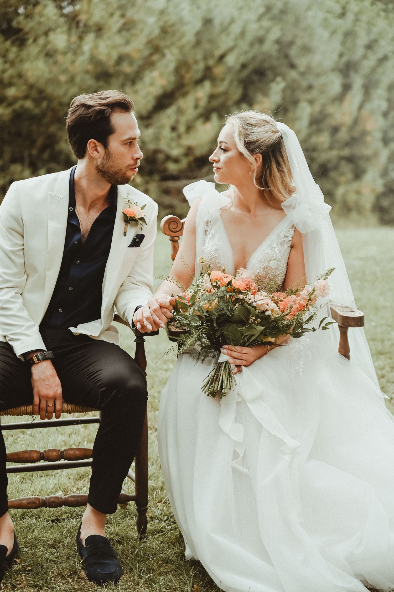 Couple shares intimate moment on rustic bench, bride holding peach and coral bouquet.