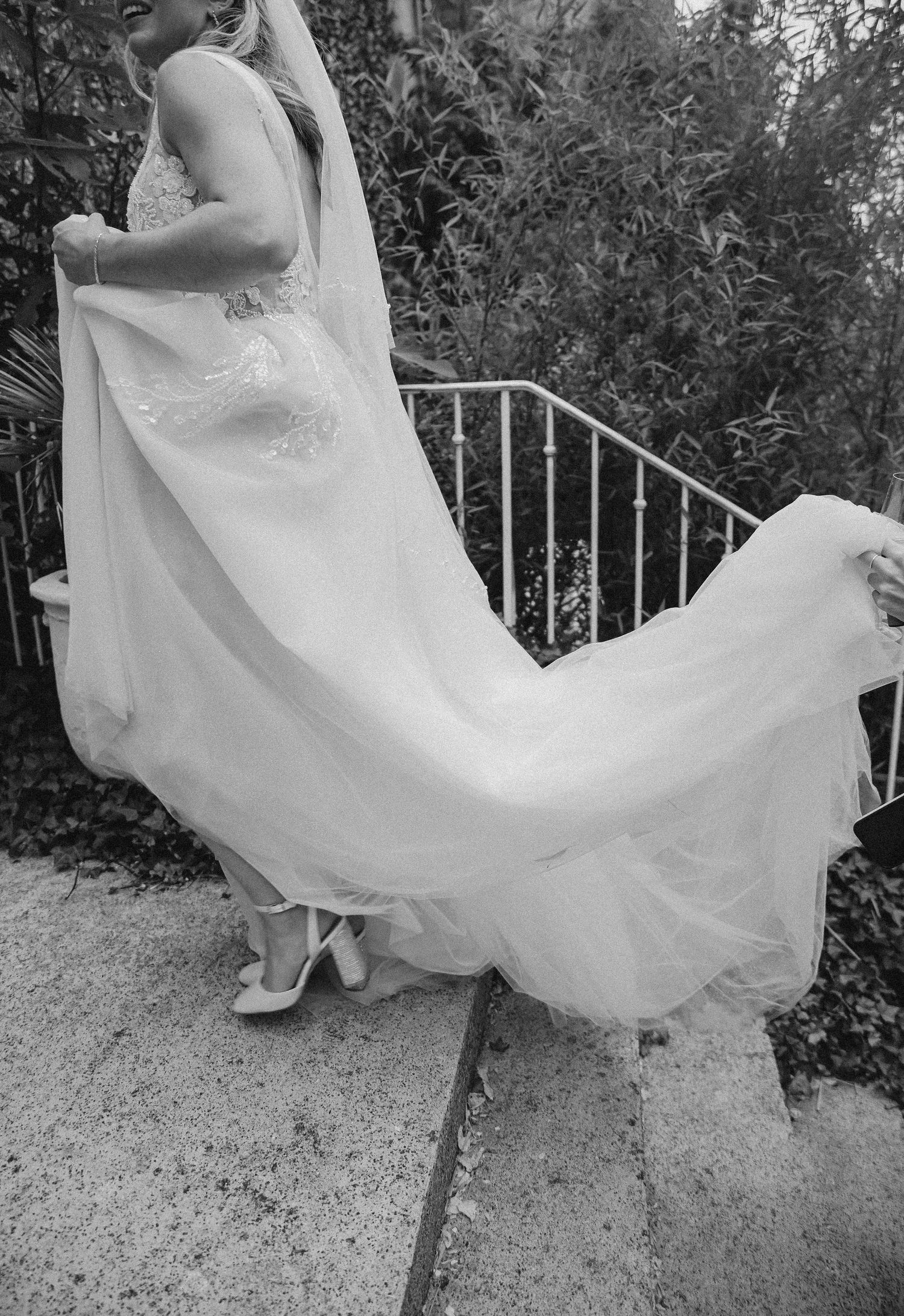Black and white photo of flowing wedding dress train and shoes on stone steps.