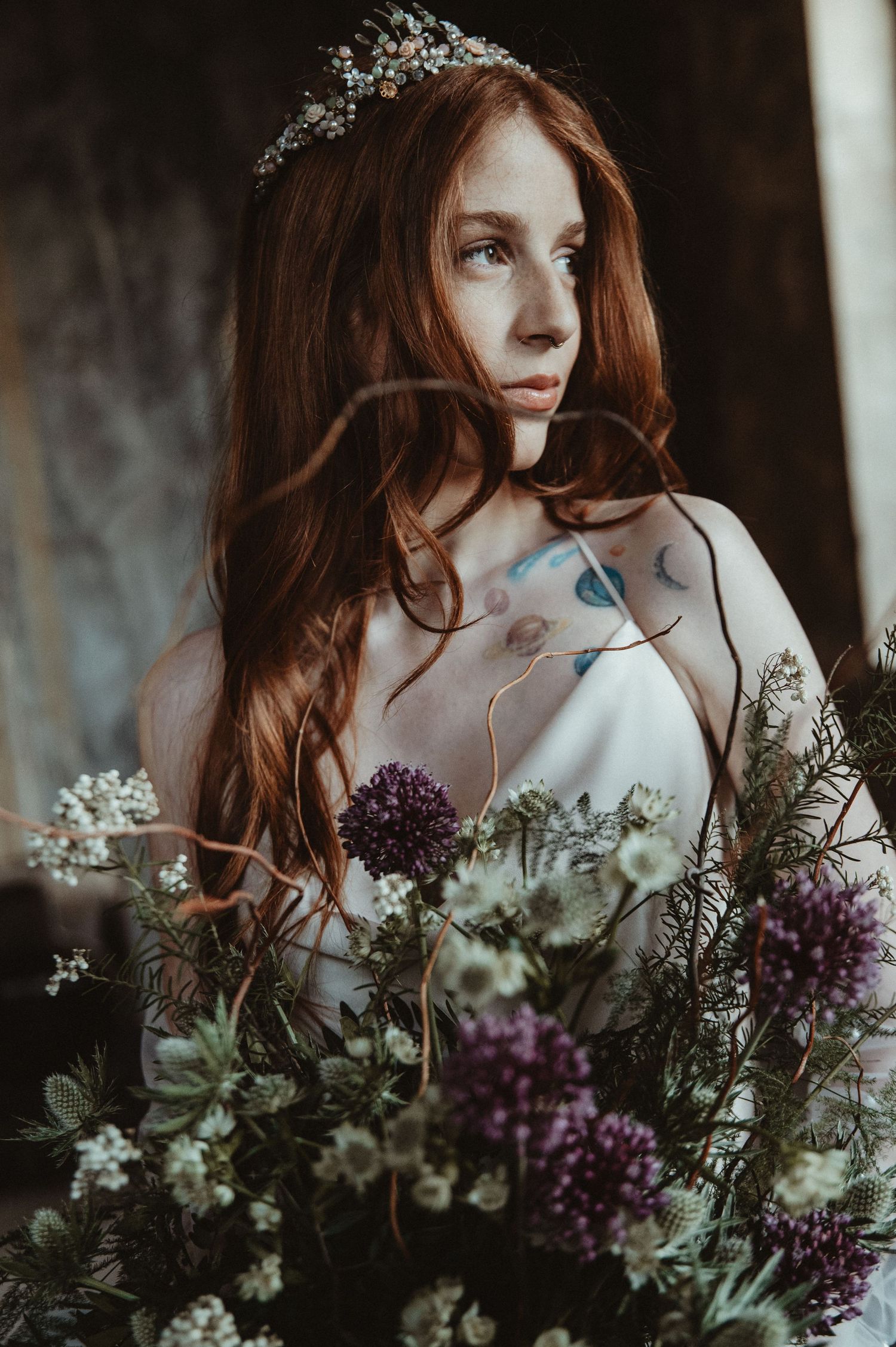Dreamy bridal portrait with crown and purple flowers against dark background.