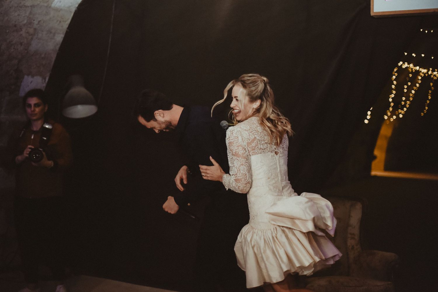 A dancing couple in vintage wedding attire enjoying a lively moment at their reception.