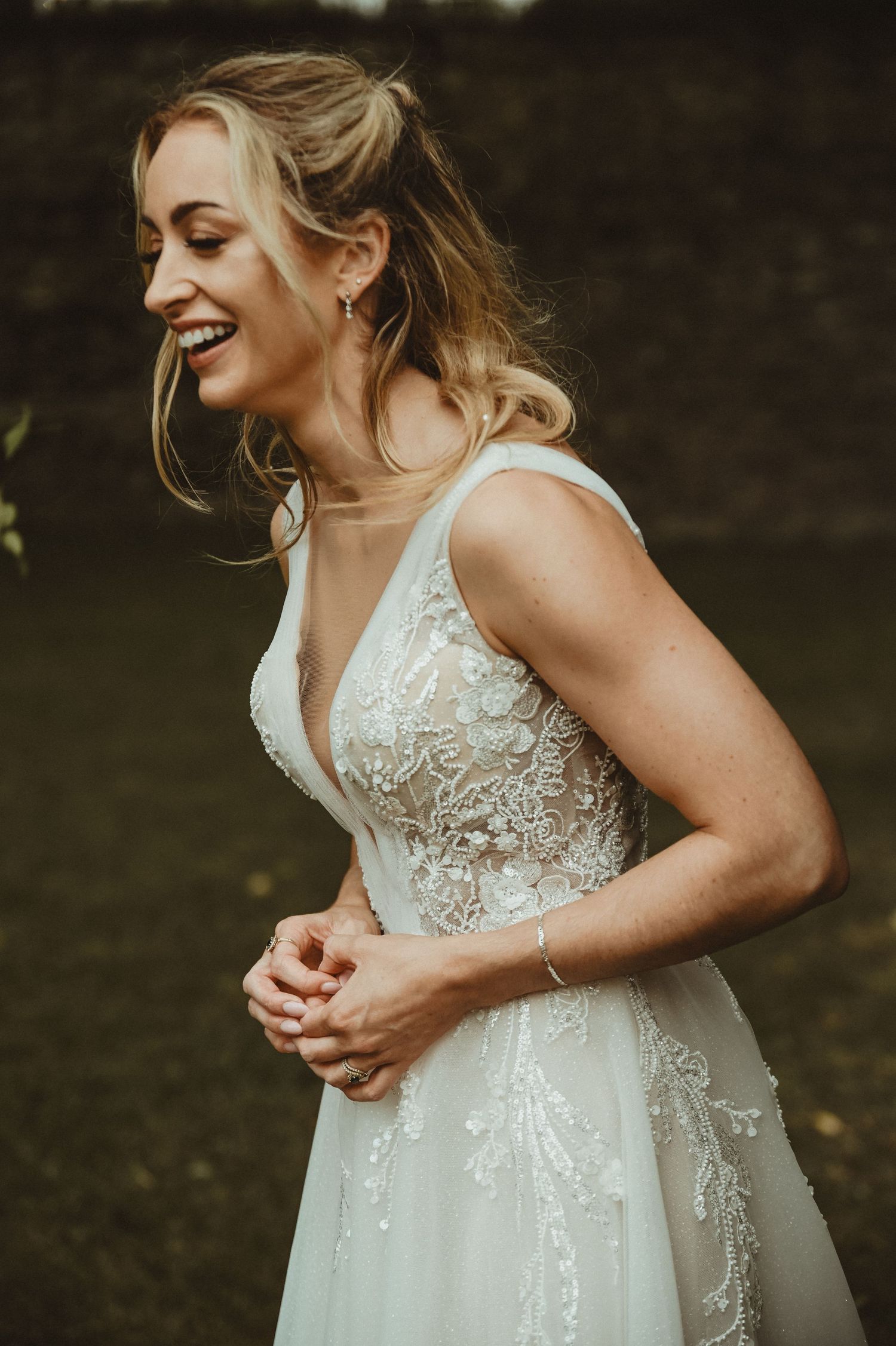 A joyful bride in a delicate lace wedding dress with a plunging neckline laughs candidly during outdoor portraits.