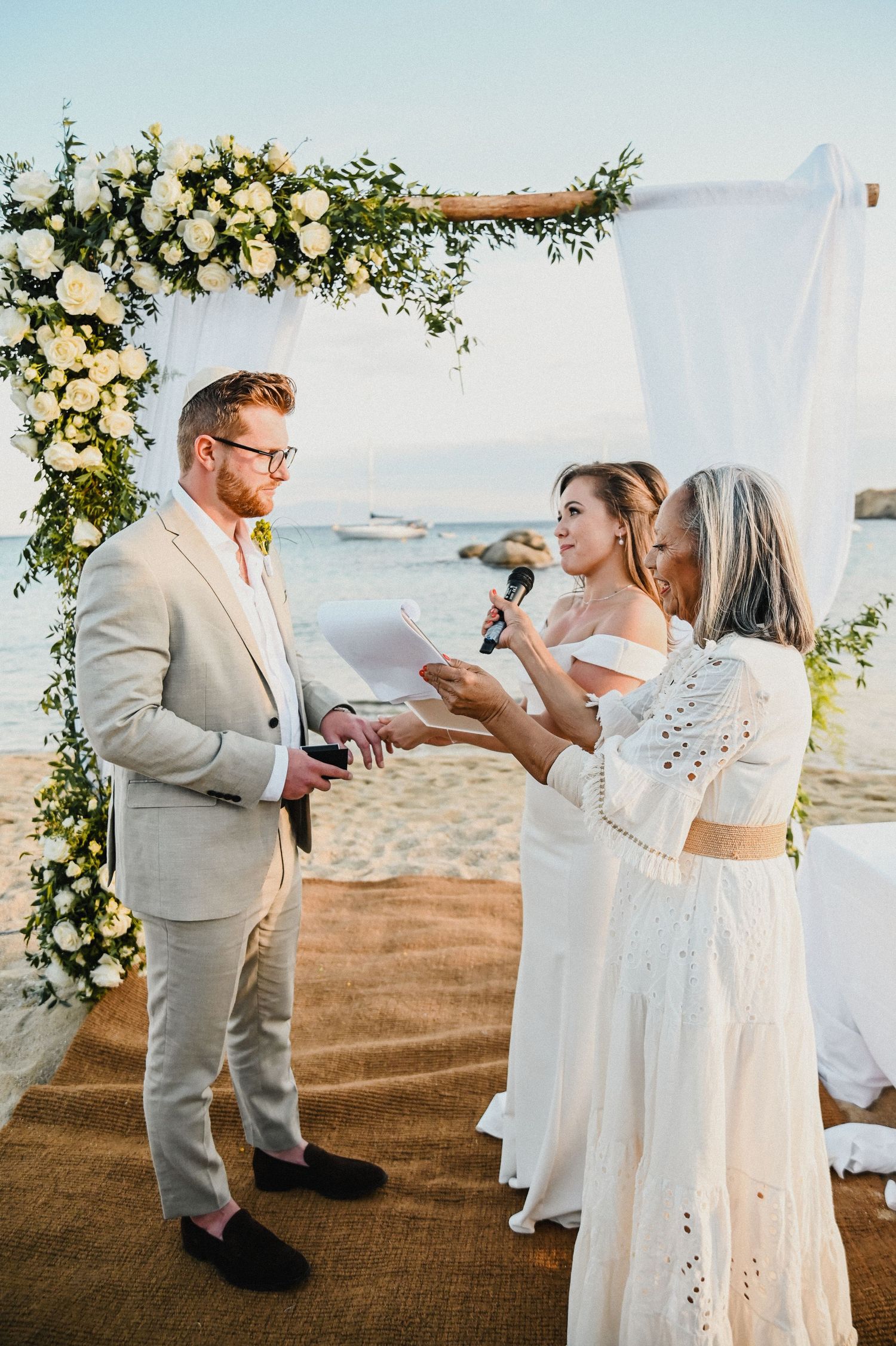 Beach wedding ceremony with elegant floral arch and exchange of rings.