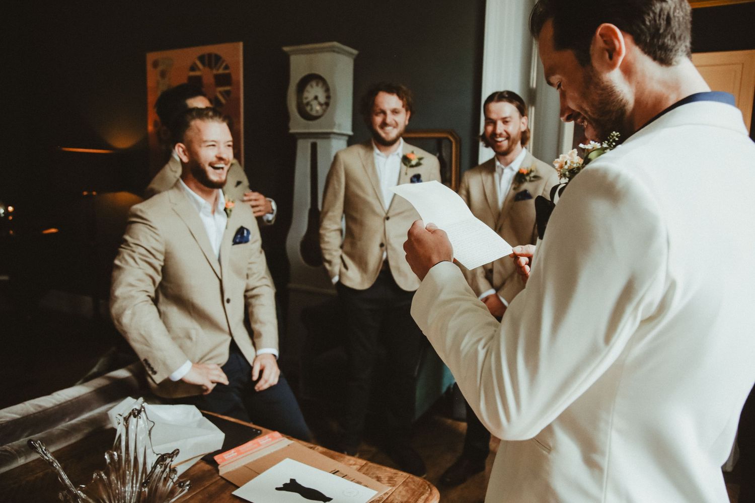 Groomsmen in beige suits gather around and share a lighthearted moment during wedding preparations.