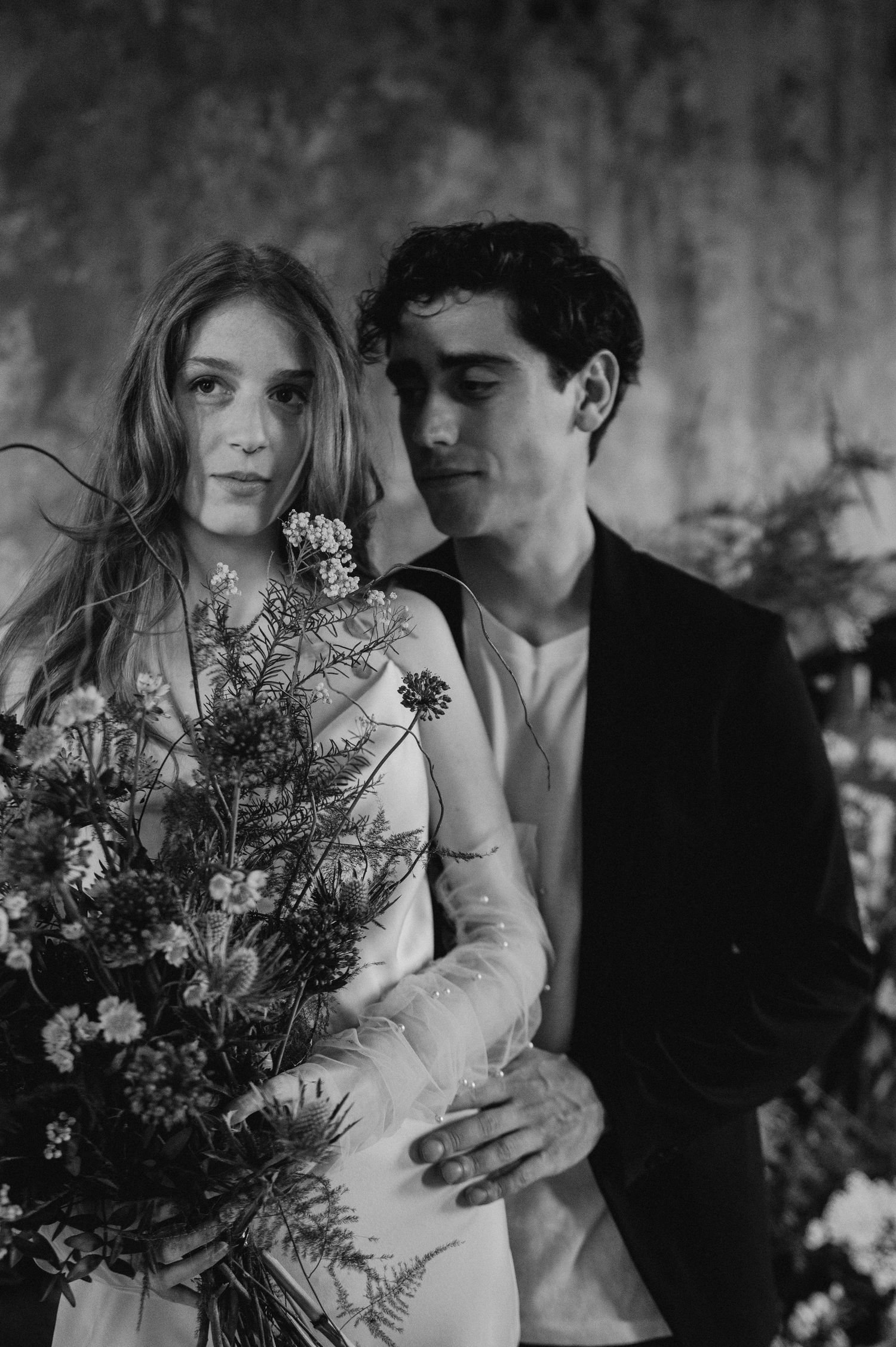 Artistic black and white portrait of a couple with a wild flower bouquet in a romantic embrace.