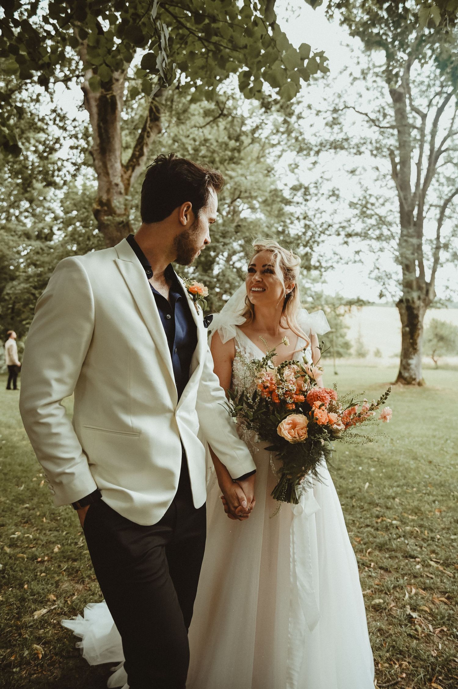 A newlywed couple shares a joyful moment outdoors, with the bride holding a vibrant orange and pink bouquet.