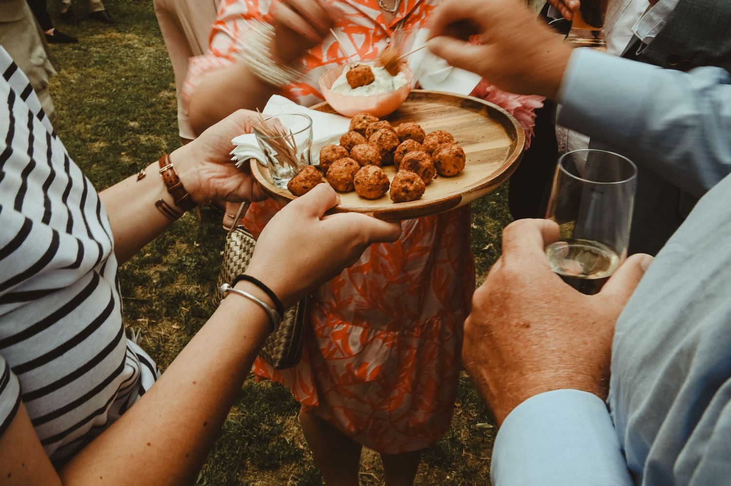 Guests sharing appetizers and drinks at outdoor wedding reception.