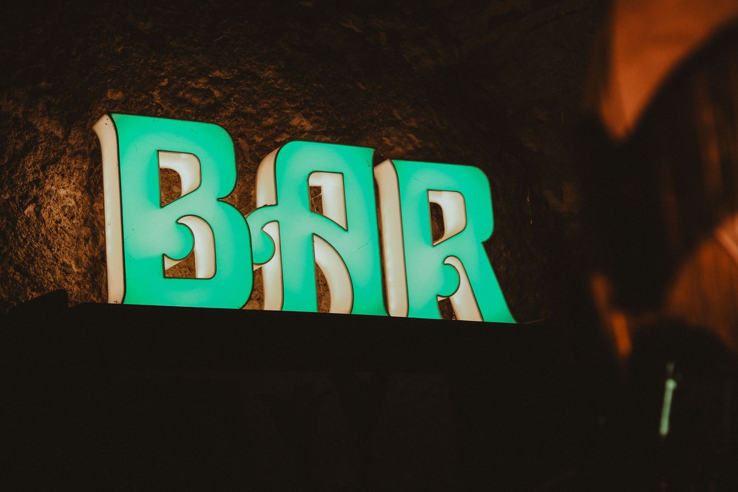 Green neon 'BAR' sign glowing against a dark stone wall.