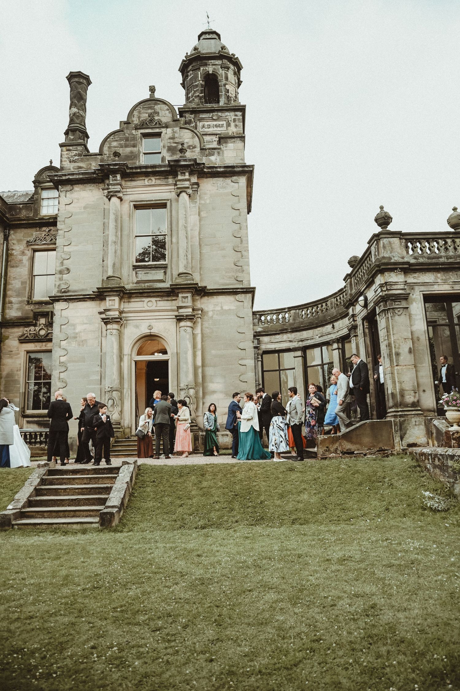Wedding guests gathering outside a grand Scottish baronial style mansion with ornate architecture.