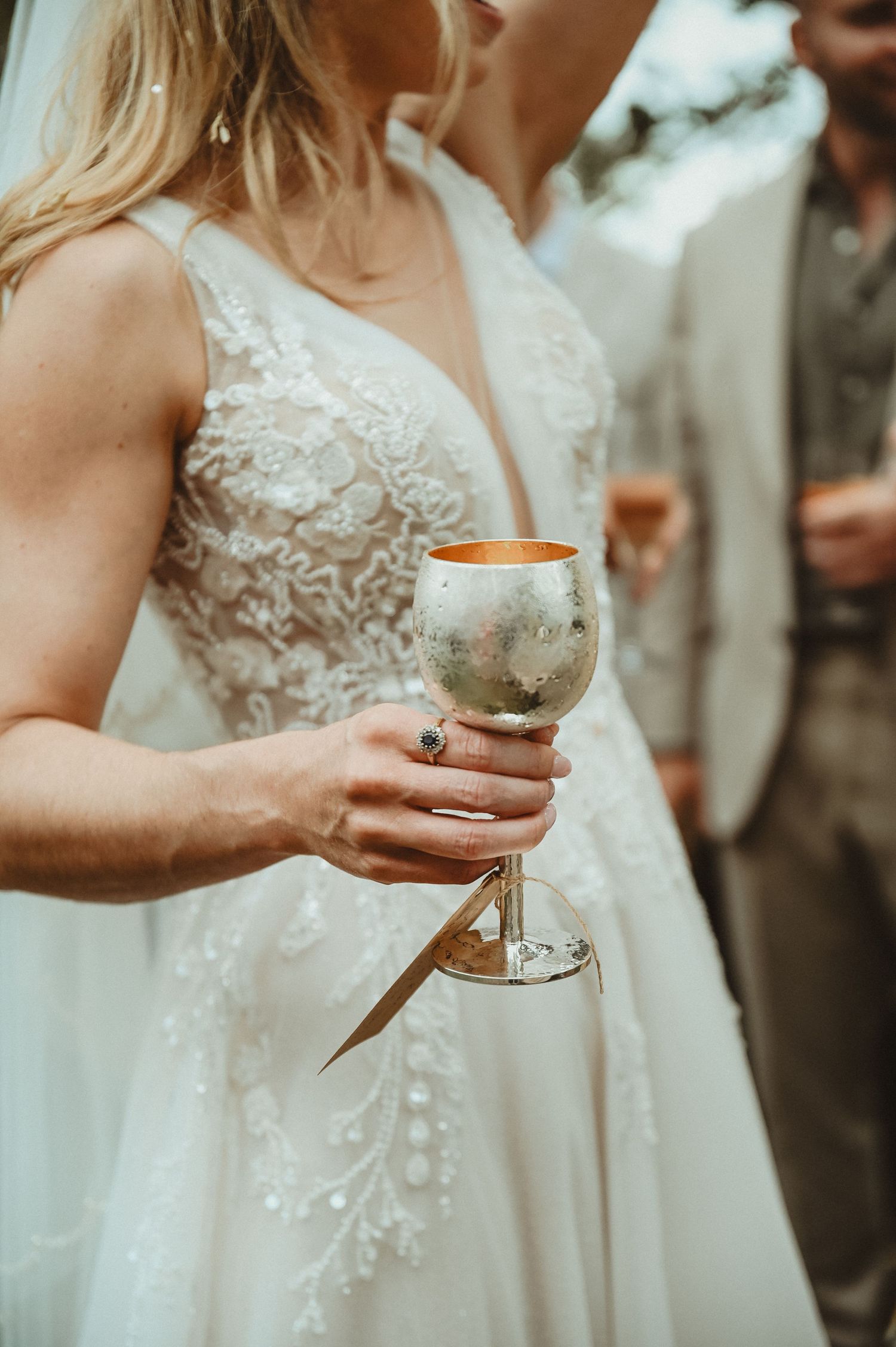 Close-up of wedding dress details and champagne glass held by person in bridal gown.