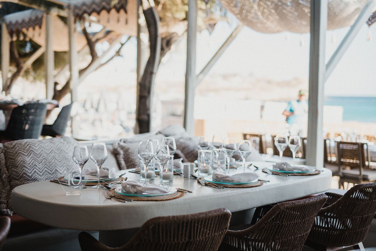 Beachside dining tables set with glasses and plates in natural lighting.
