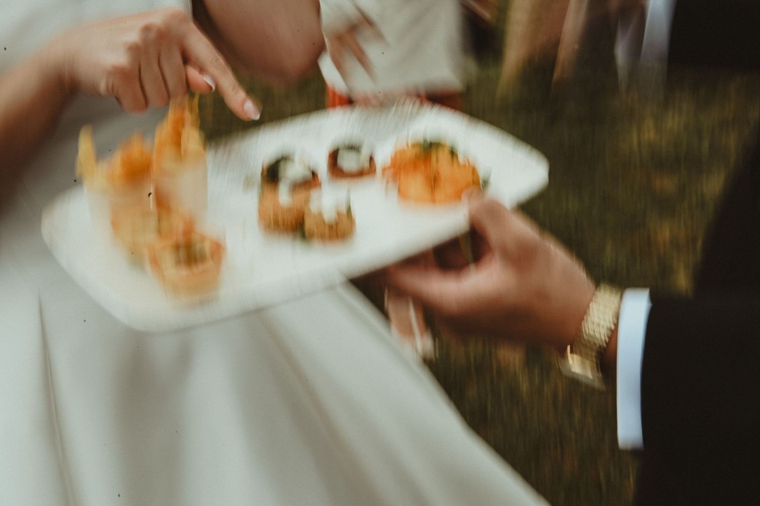 Close-up of hands holding plate of appetizers at outdoor event.