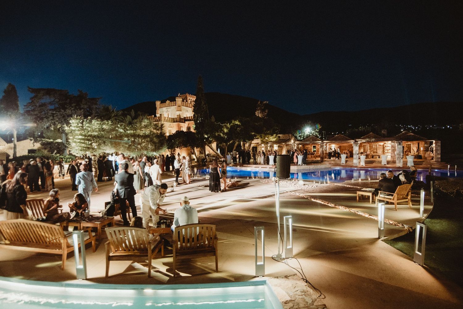 Nighttime outdoor wedding reception with illuminated castle backdrop.
