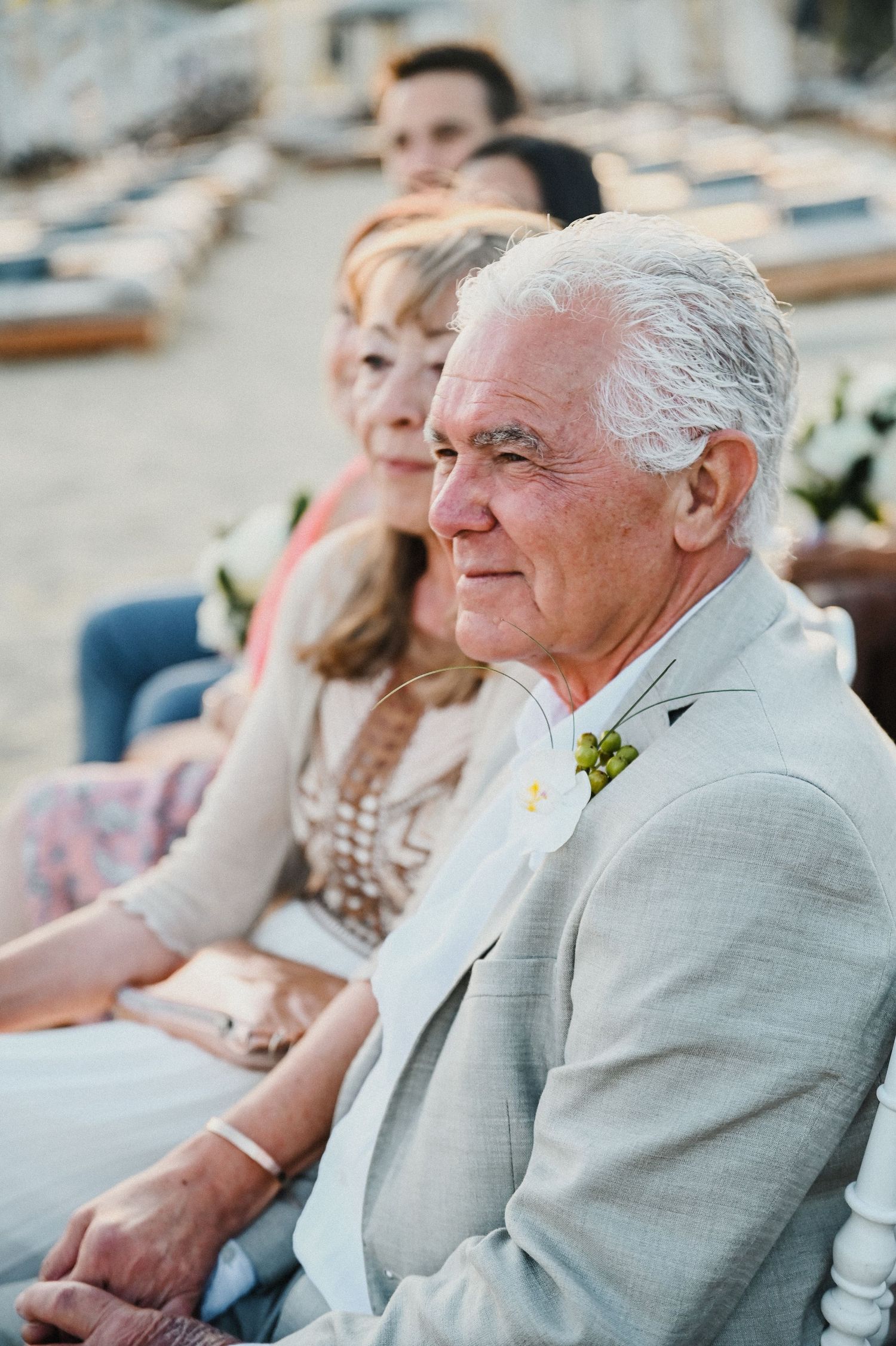 Wedding guest in light gray suit watches ceremony with a warm smile.