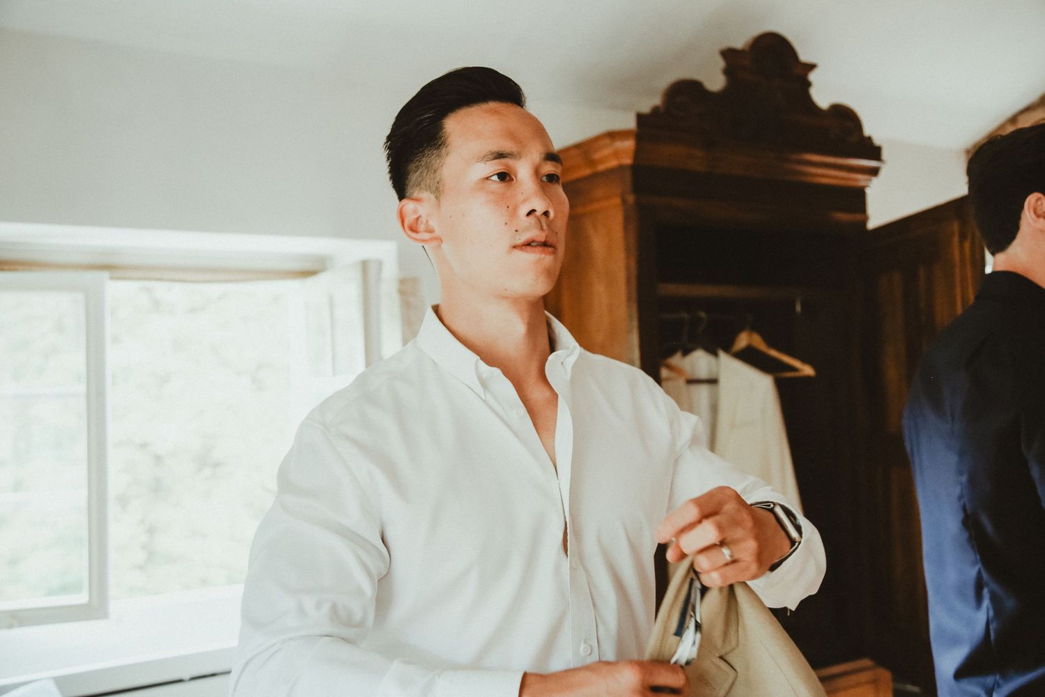 Person adjusts their white dress shirt while getting ready in a sunlit room.
