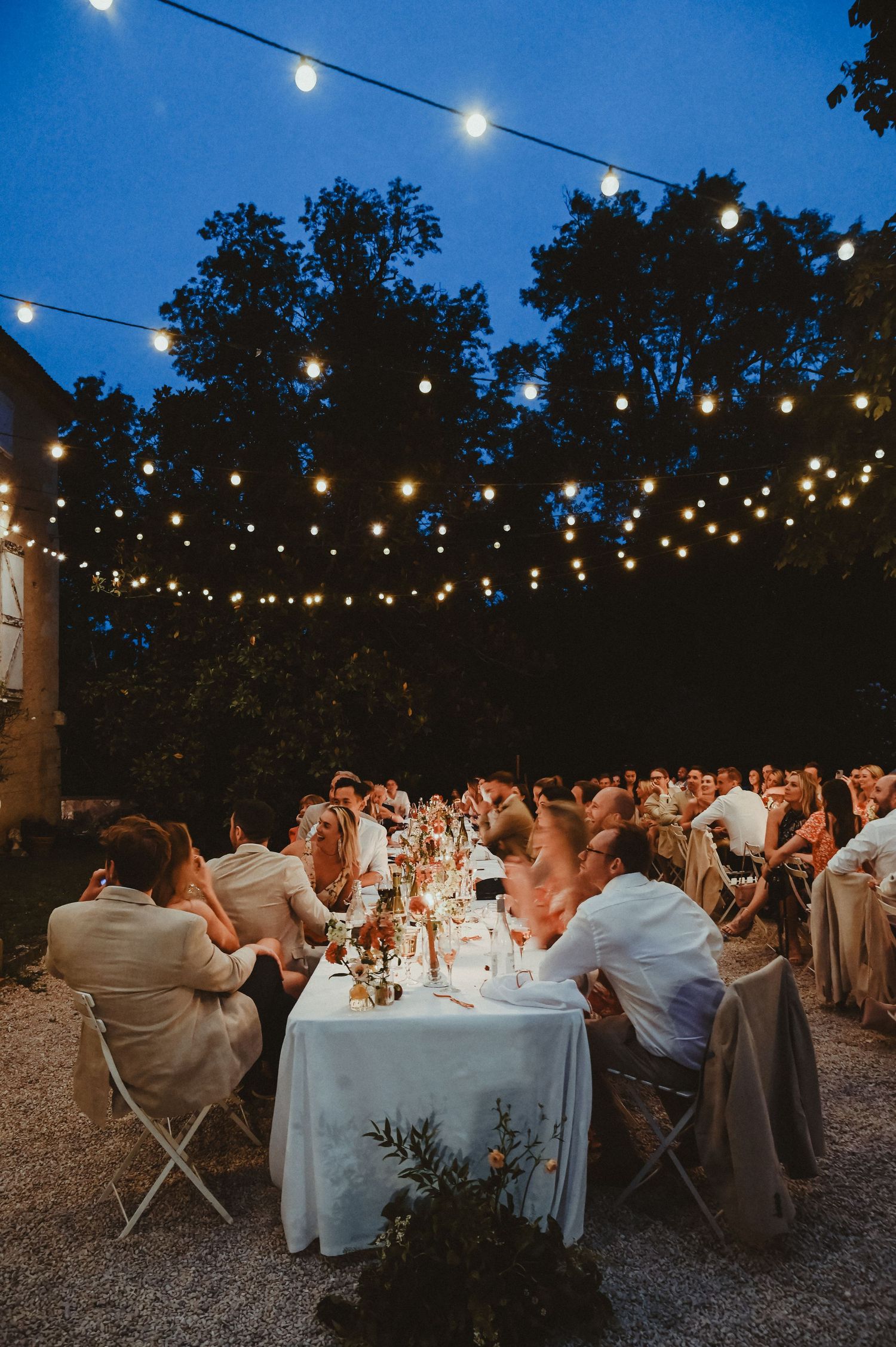 Romantic evening wedding reception under canopy of string lights with elegant table settings.
