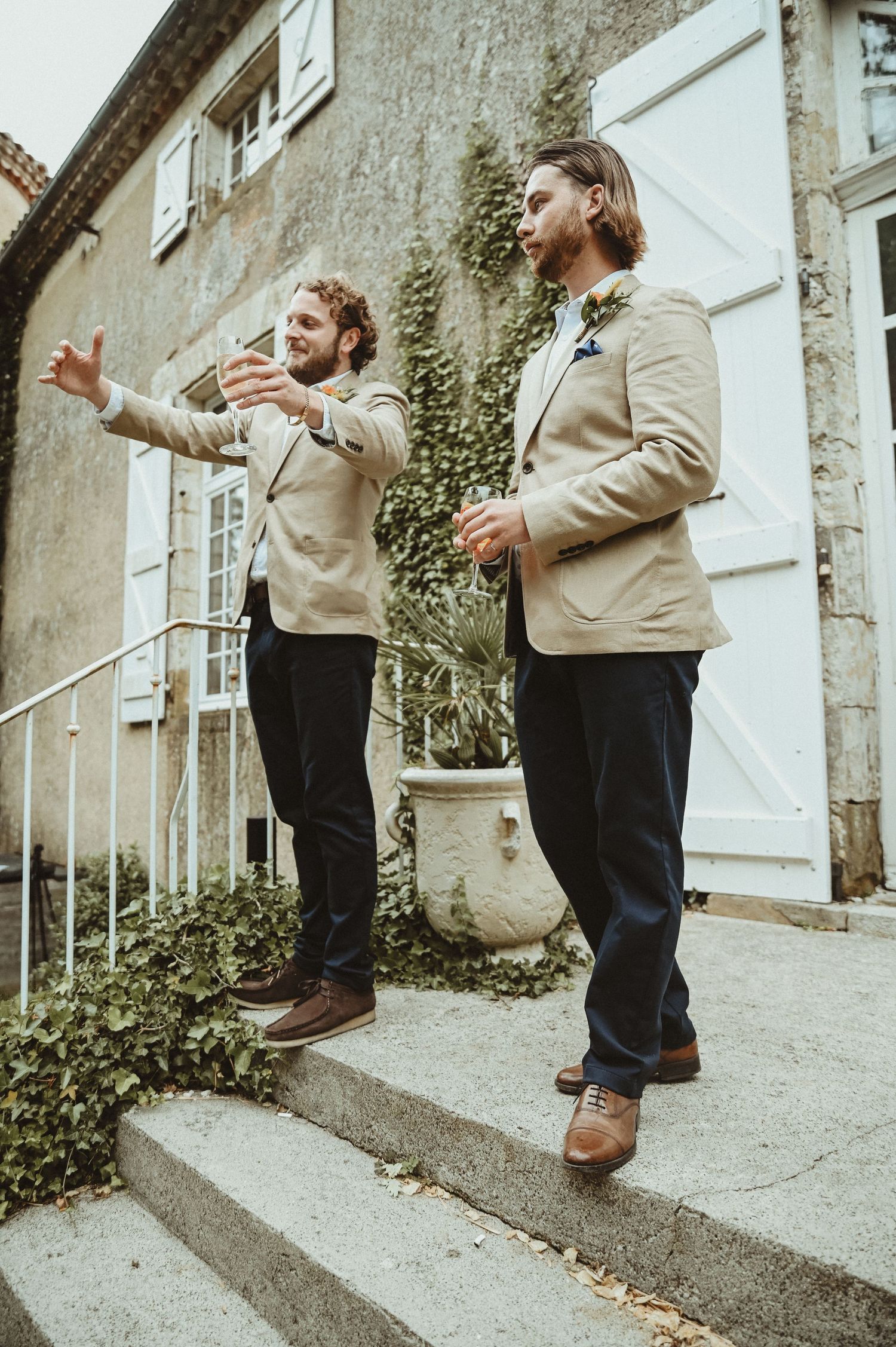 Two men in beige jackets gesture animatedly while standing on stone steps.