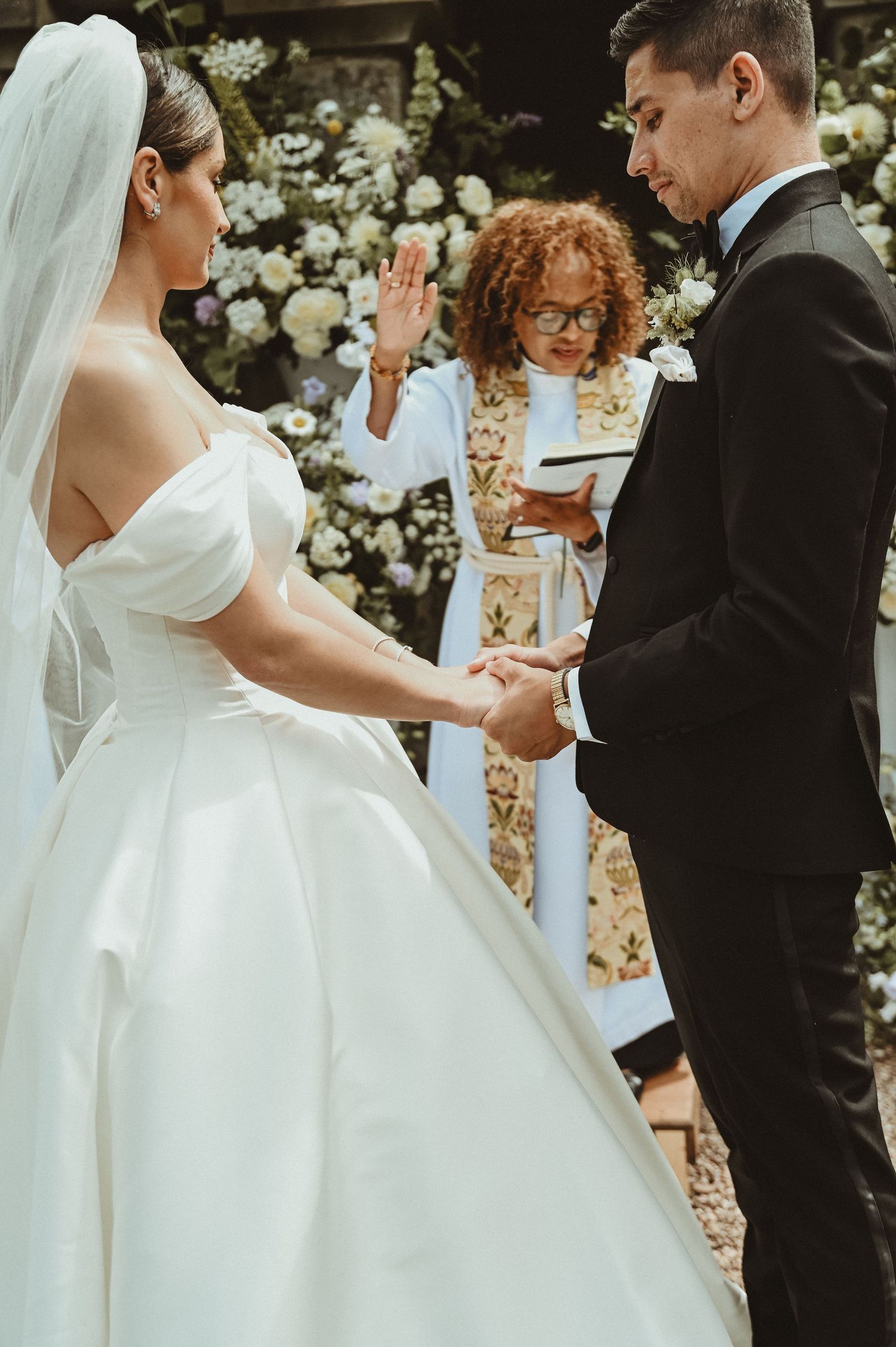A wedding ceremony in progress beneath a stone archway with elegant floral decorations.