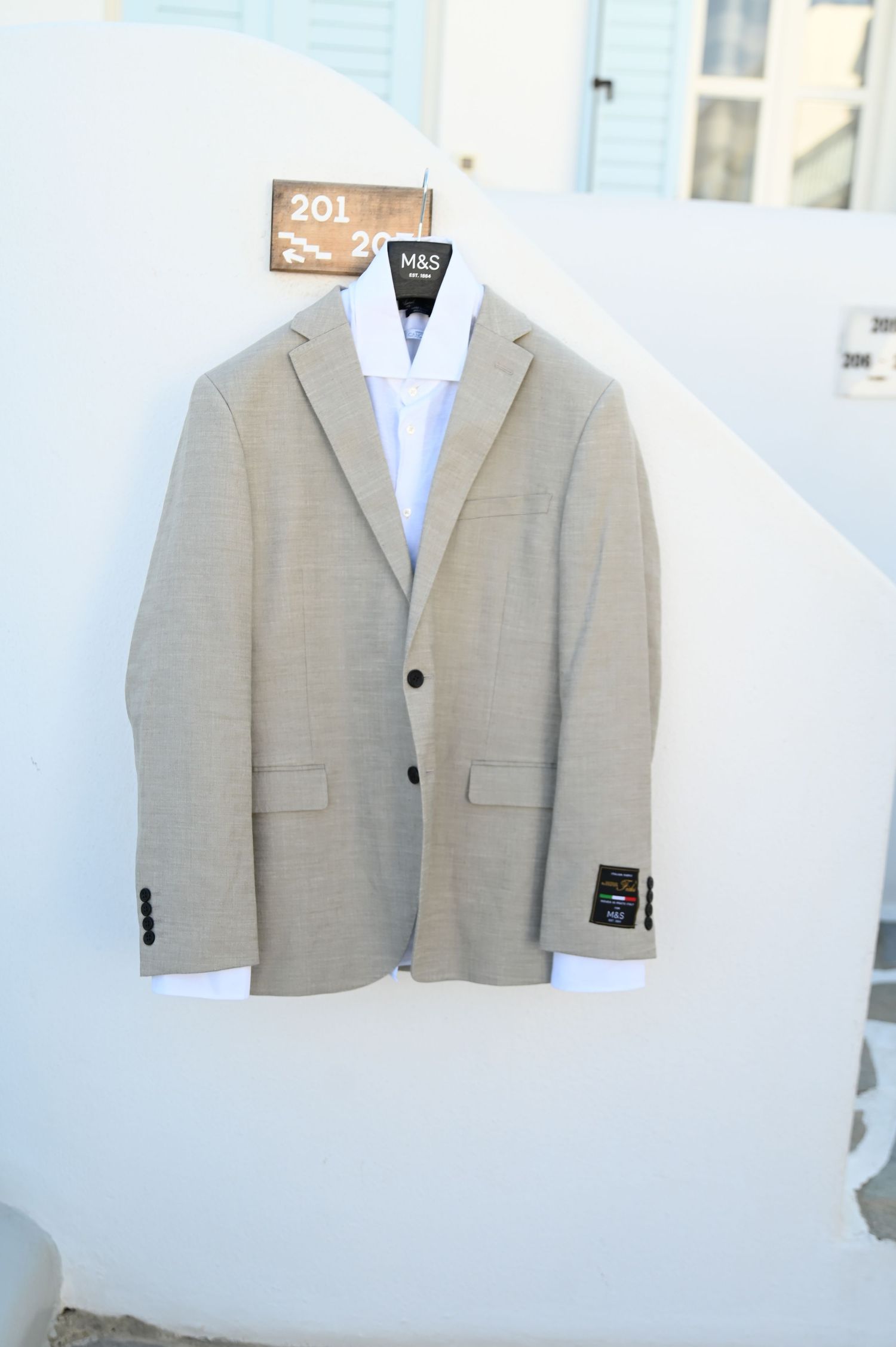 Light gray suit jacket hanging against a white wall with a blue dress shirt underneath.