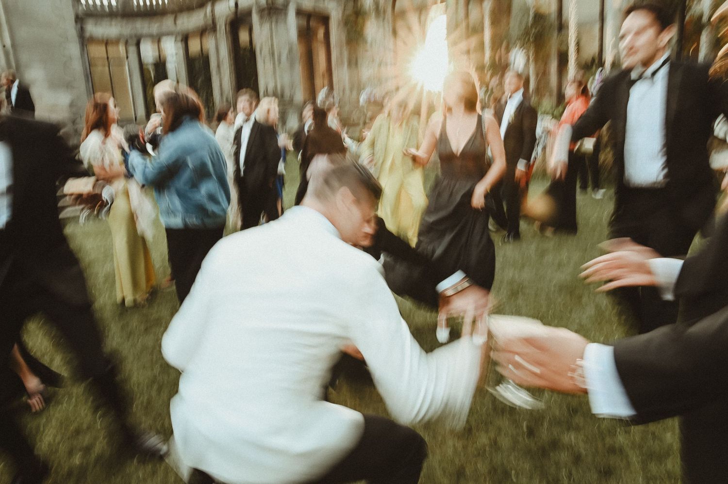Motion-blurred candid shot of wedding guests dancing at an outdoor celebration.