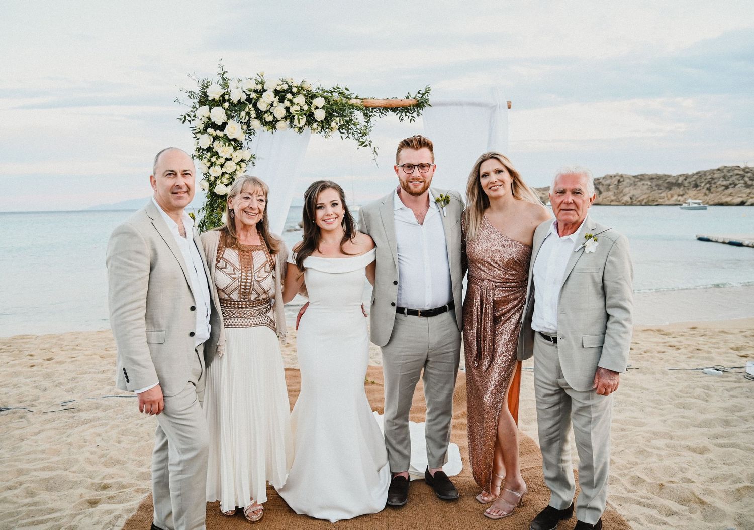 Small family group photo under floral wedding arch on beach setting.