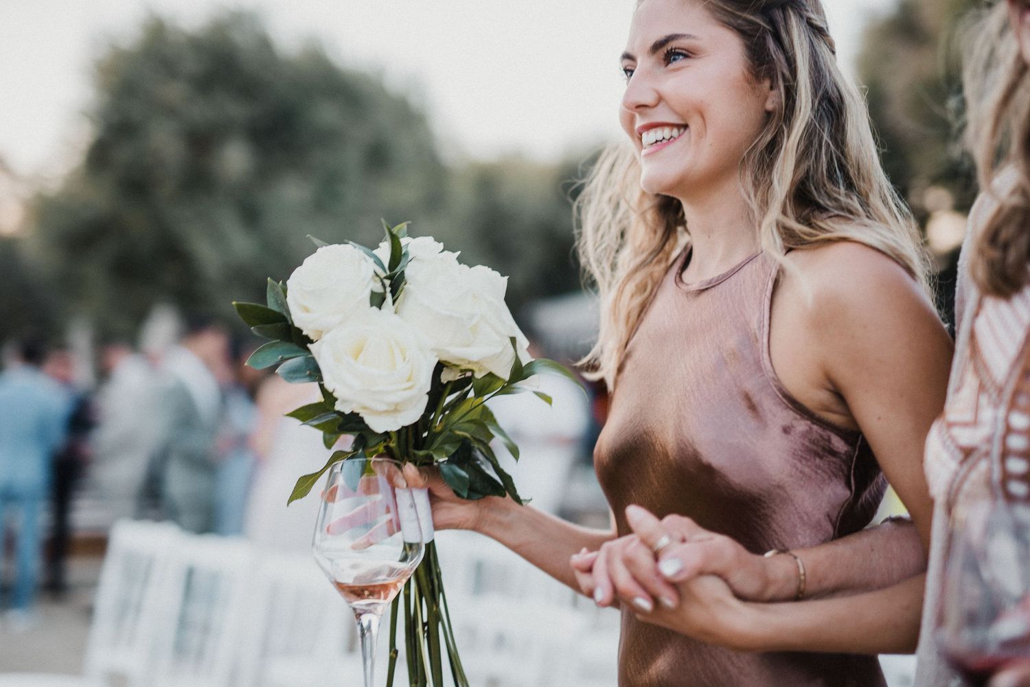 Wedding attendee holding white rose bouquet at outdoor celebration.