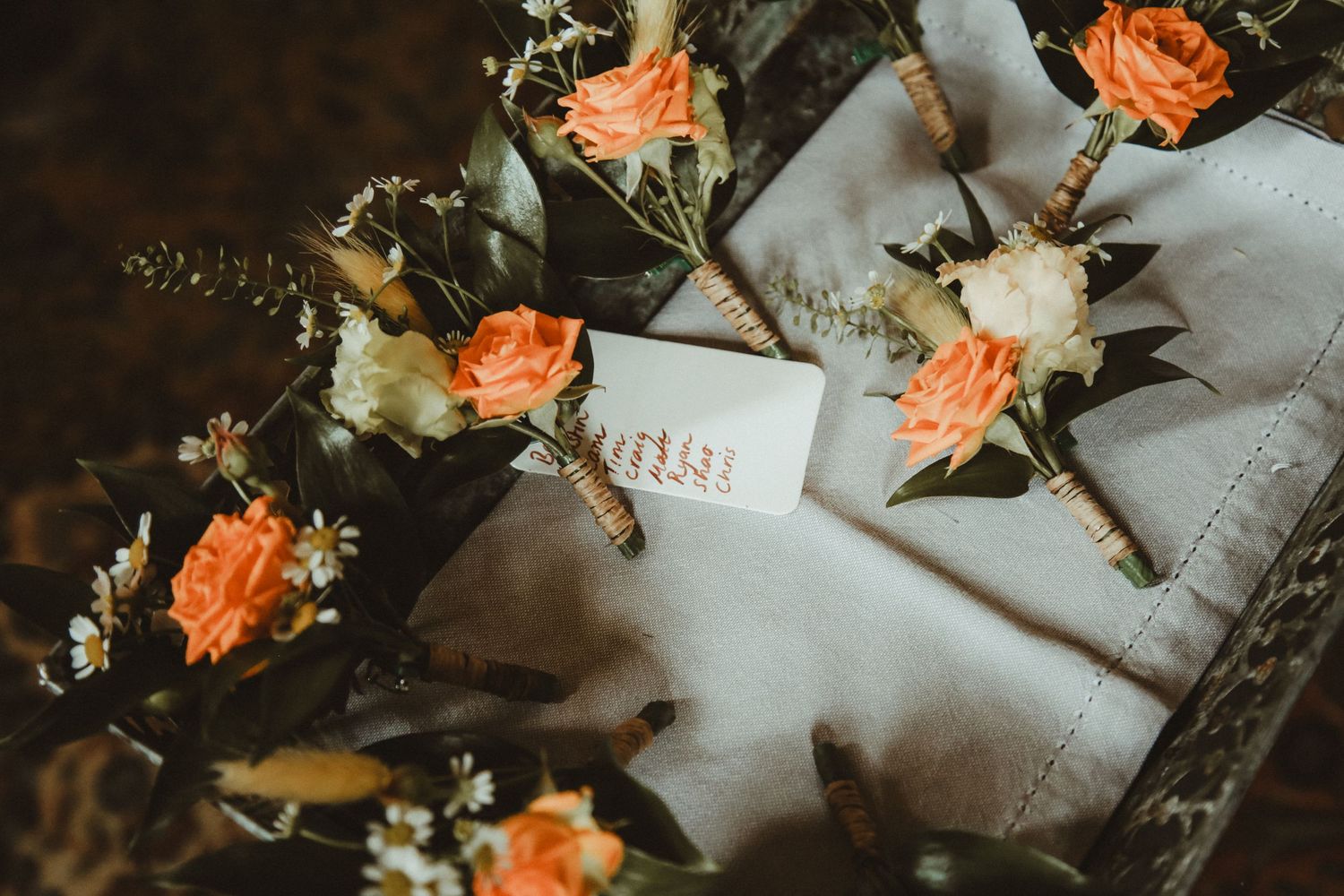 Delicate peach roses arranged as boutonnieres with greenery on white fabric.