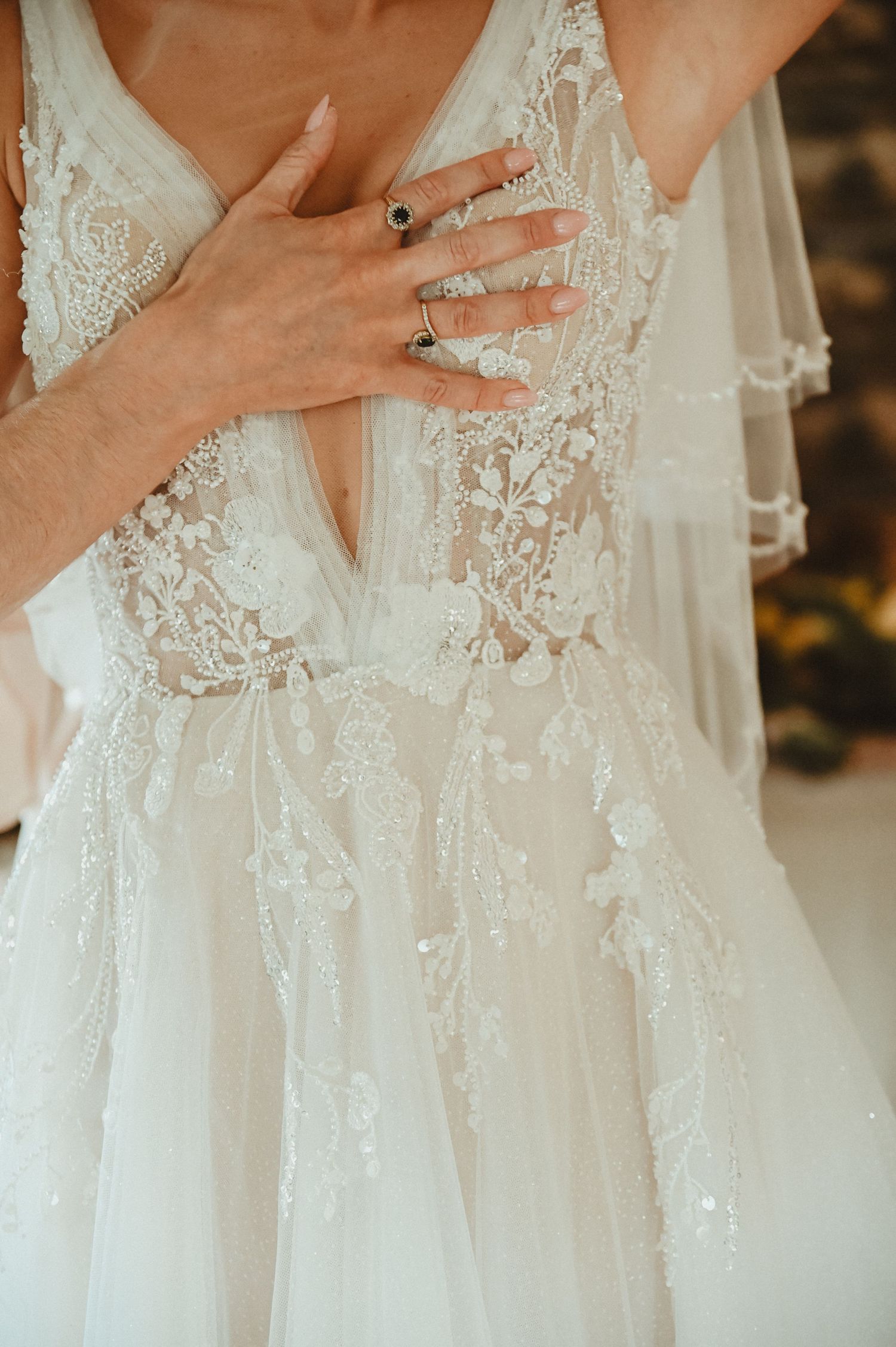 Detailed close-up of delicate lace wedding dress bodice with hand showing ring.